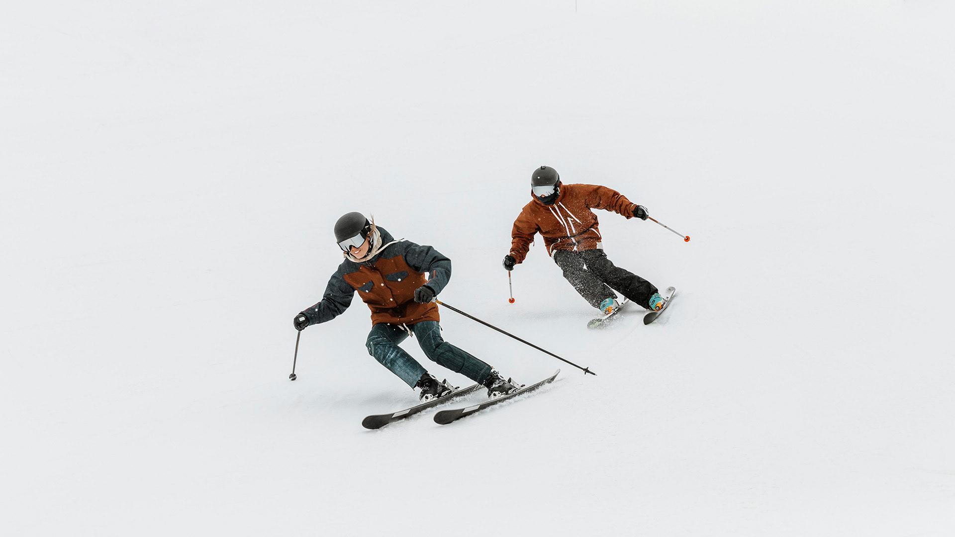 Cuts to wide shot showing friends wearing the Alpine Smart Goggles going down the hill rapidly. Friend 1 is going down the hill as friend 2 follows behind. Audience sees more of Friend 2 introducing them for the next shot. Laughing and woosh sound effects play as they pass.