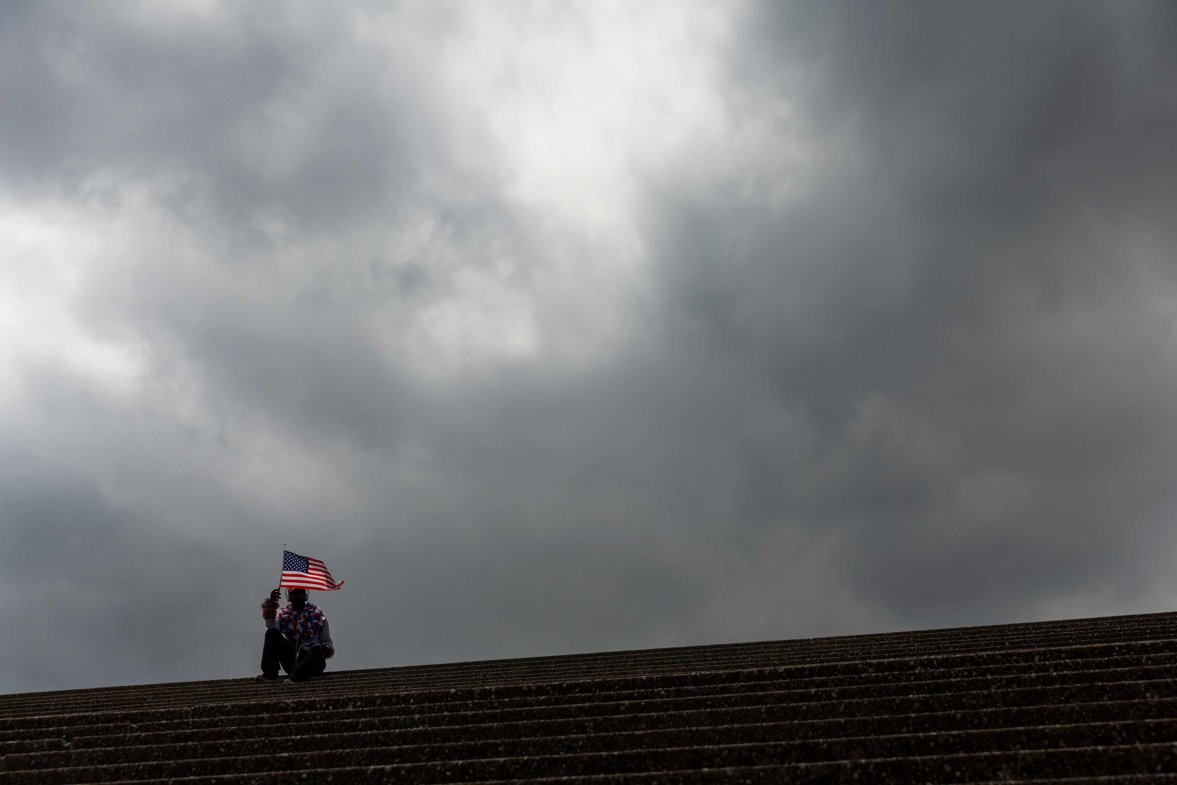 With flag in hand, Tim Crusoe of St. Louis, Mo., sits under the Gateway Arch in anticipation of the Fourth of July annual celebration at Gateway Arch National Park in St. Louis. "I love Fourth of July. It's my favoritest holiday ever," Crusoe said. 