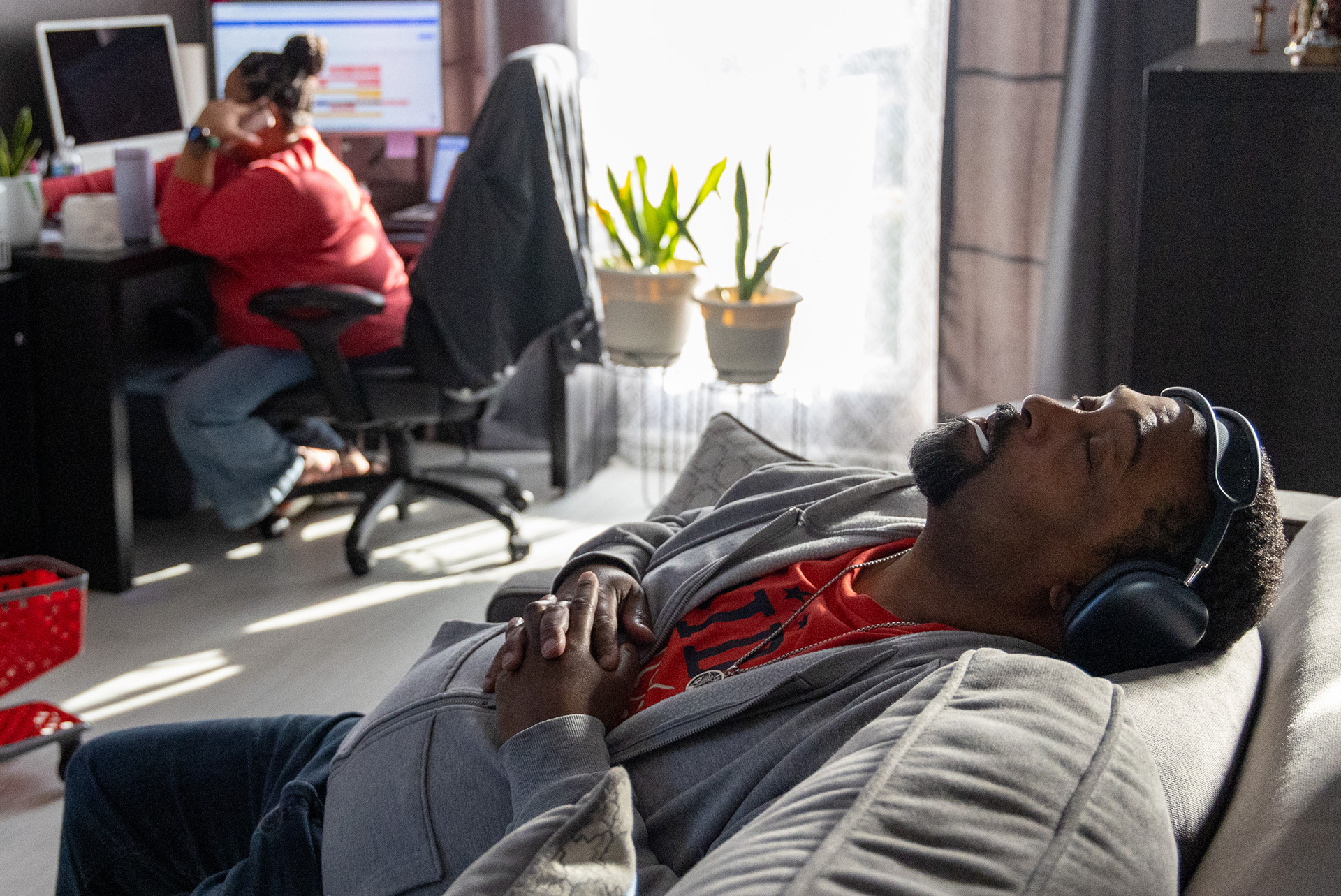 After an overwhelming morning getting his young daughters ready for school and grocery shopping, Tony Walker, right, relaxes on the couch listening to Gospel rap while his wife Rosemary Walker works, Thursday, Sept. 4, 2025, at their home in Plainfield. Walker explained that after his stroke and heart disease diagnosis he is easily mentally overwhelmed and has to take frequent breaks to relax. His wife has become his full-time caretaker and he often sits on the couch next to her while she works. (Dominic Di Palermo/ Chicago Tribune)