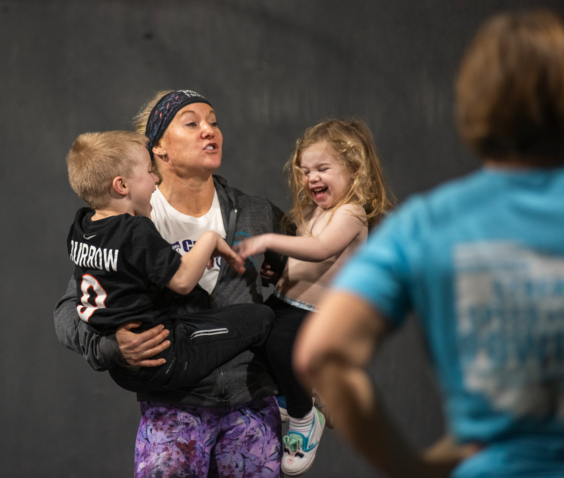 Owner Jolene Quirke, holding her kids, Colt (left) and JoElaine Quirke (right) while discussing the workout during group class, at CrossFit SEO, in Athens, Ohio, Dec. 2, 2023. Quirke is a mom of three, and it is very difficult for her as a mom, owning a gym and working many hours at CrossFit SEO. “I do love what I do, but I do feel as if I’m being pulled in many directions. I wonder if I’m present with them enough as that is my number one priority,” Quirke said.