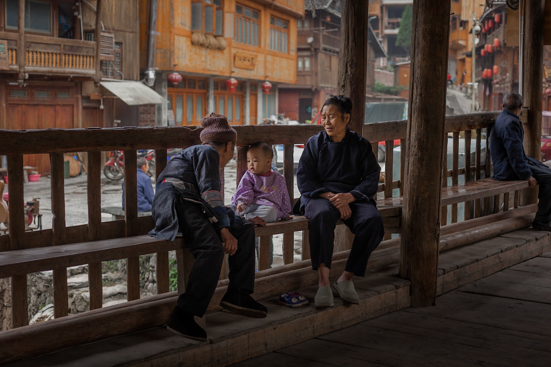 Mother, child and elder sit on benches on covered bridge