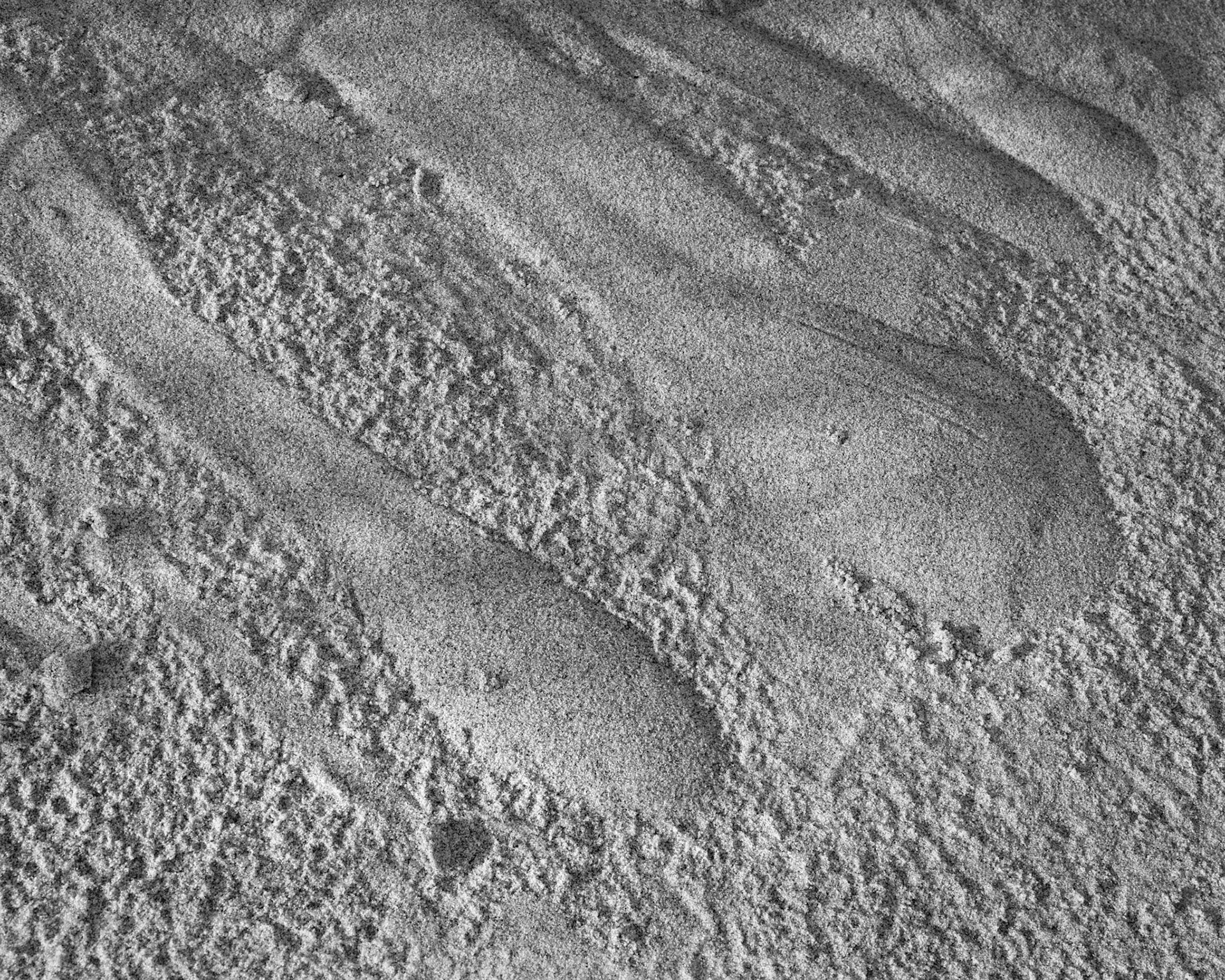 Dry wind-blown sand, captured into a small hill at the base of a clump of grass, cascades sown over the rain-dimpled surface below - a landslide in miniature.  I sm not in danger from this geological process because scale matters.