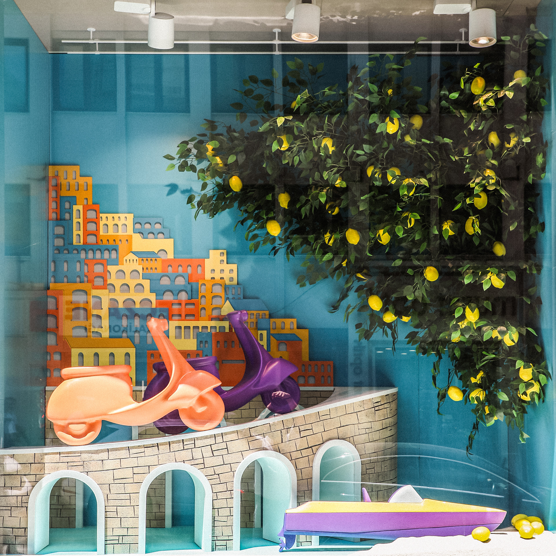 Photograph of the completed screen installation in a textile brand’s retail space, featuring sculptural forms, bold colors, a lemon tree, and a layered summer-themed backdrop.