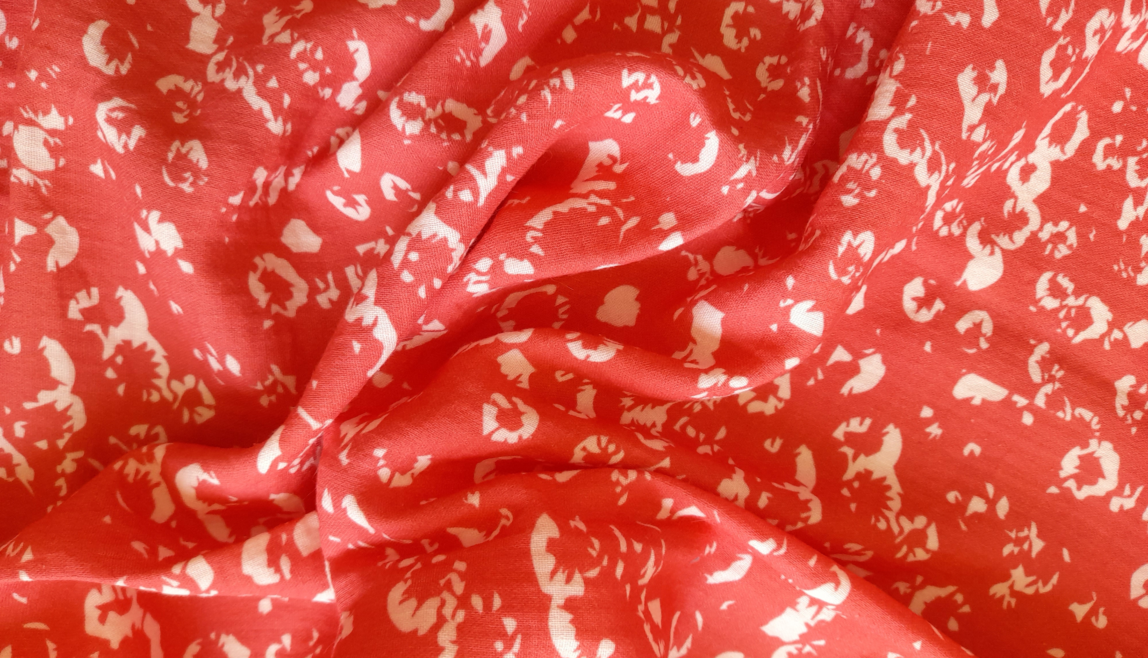 Coral red fabric printed with abstract white floral pattern, softly draped to show texture and flow.