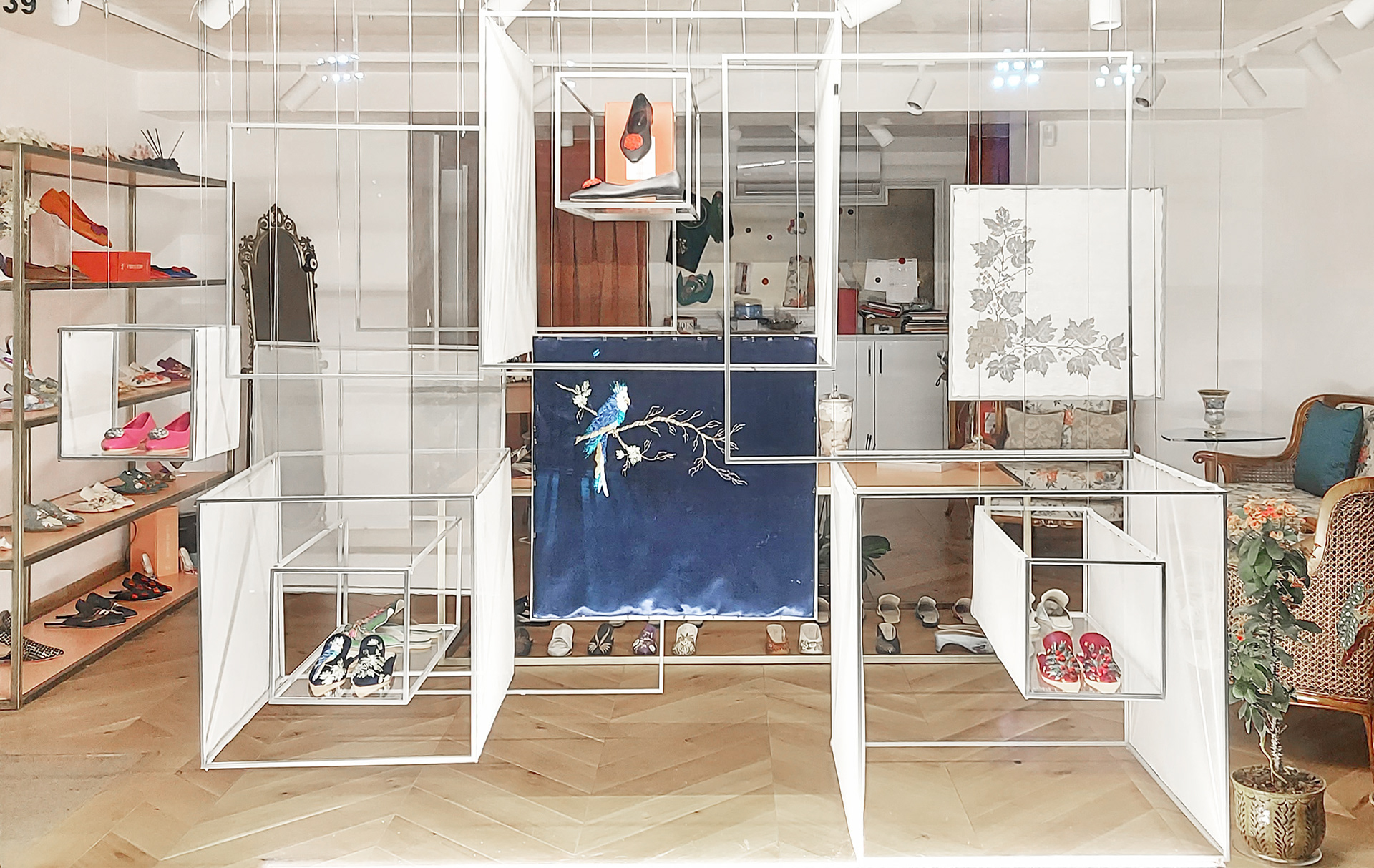 Daytime photo of the window display featuring a grid of white frames and textile panels inspired by embroidery, showcasing shoes in a boutique setting.