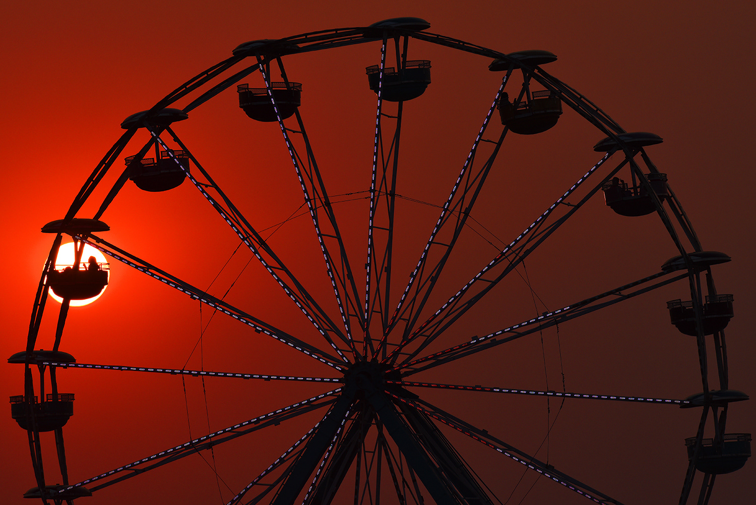 A single rider is silhouetted by the setting sun on the ferris wheel on Thursday, Aug. 9, 2018, at the Umatilla County Fair in Hermiston, Oregon. Smoke from wildfires throughout the Pacific Northwest hands in the air casting the light from the setting sun in a dark red hue. 