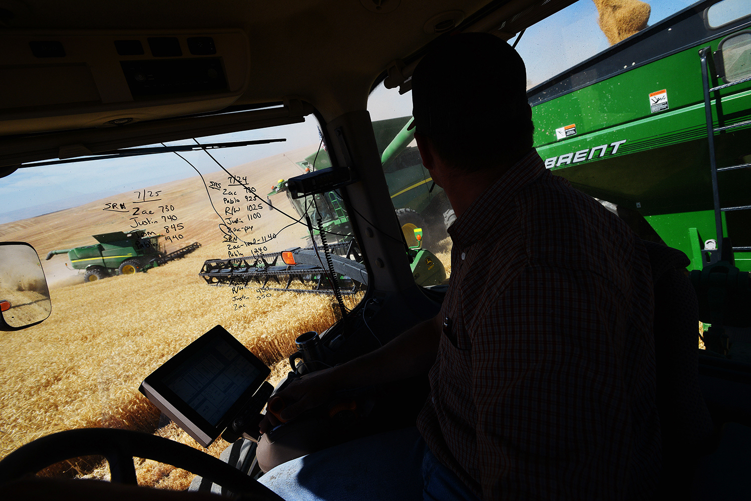 Bank-out wagon driver Casey Evans lines up to take a load of wheat from a combine as another combine harvests wheat in a field Tuesday, July 7, 2017, outside of Helix, Oregon. The numbers written on the window of the cab shows the bushels of wheat harvested by each combine.
