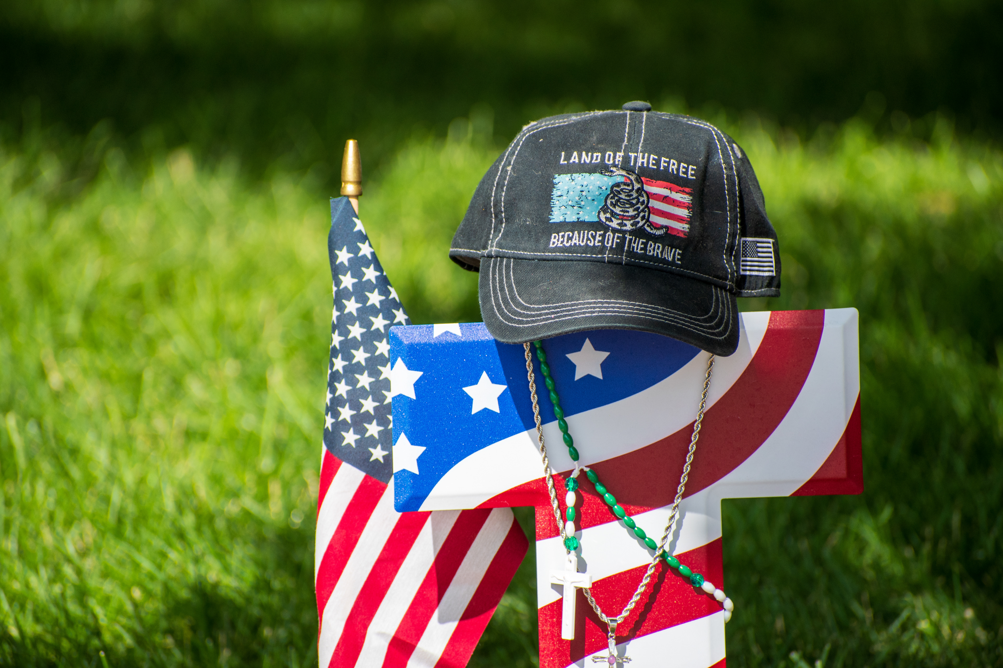 OREM, UTAH – SEPTEMBER 15, 2025: A cross wrapped in an American flag design is seen at a memorial honoring Charlie Kirk on the campus of Utah Valley University. A black baseball cap reading “LAND OF THE FREE BECAUSE OF THE BRAVE” rests atop the cross, alongside a small flag and a silver necklace with a cross pendant. © Charles‑McClintock Wilson / ZUMA Press