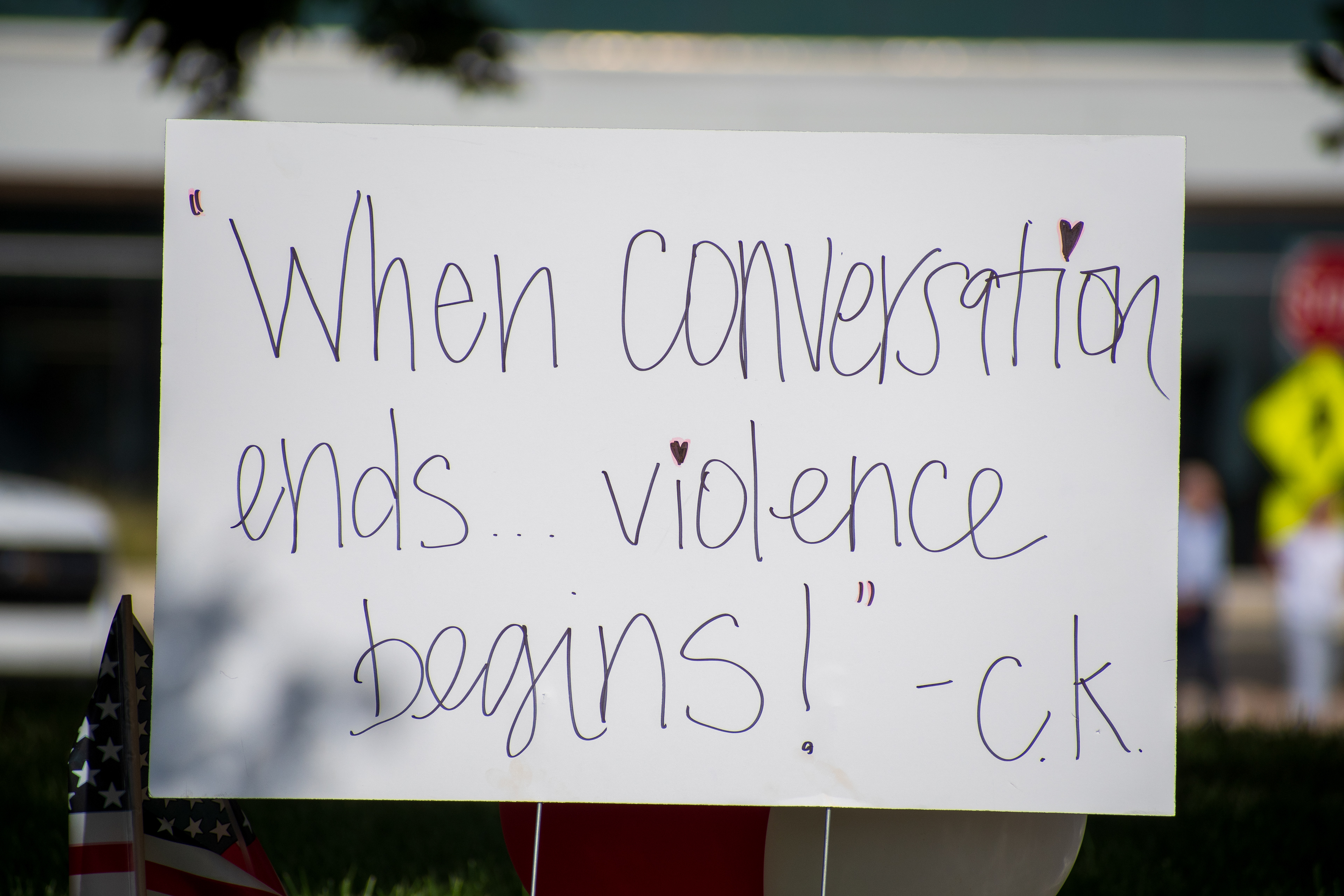 OREM, UTAH – SEPTEMBER 15, 2025: A handwritten sign reading “When conversation ends... violence begins! – c.k.” is displayed at a memorial site for Charlie Kirk on the campus of Utah Valley University. Small heart stickers decorate the sign, which is surrounded by American flags and red, white, and blue decorations. A stop sign and pedestrian crossing sign are visible in the background. © Charles‑McClintock Wilson / ZUMA Press