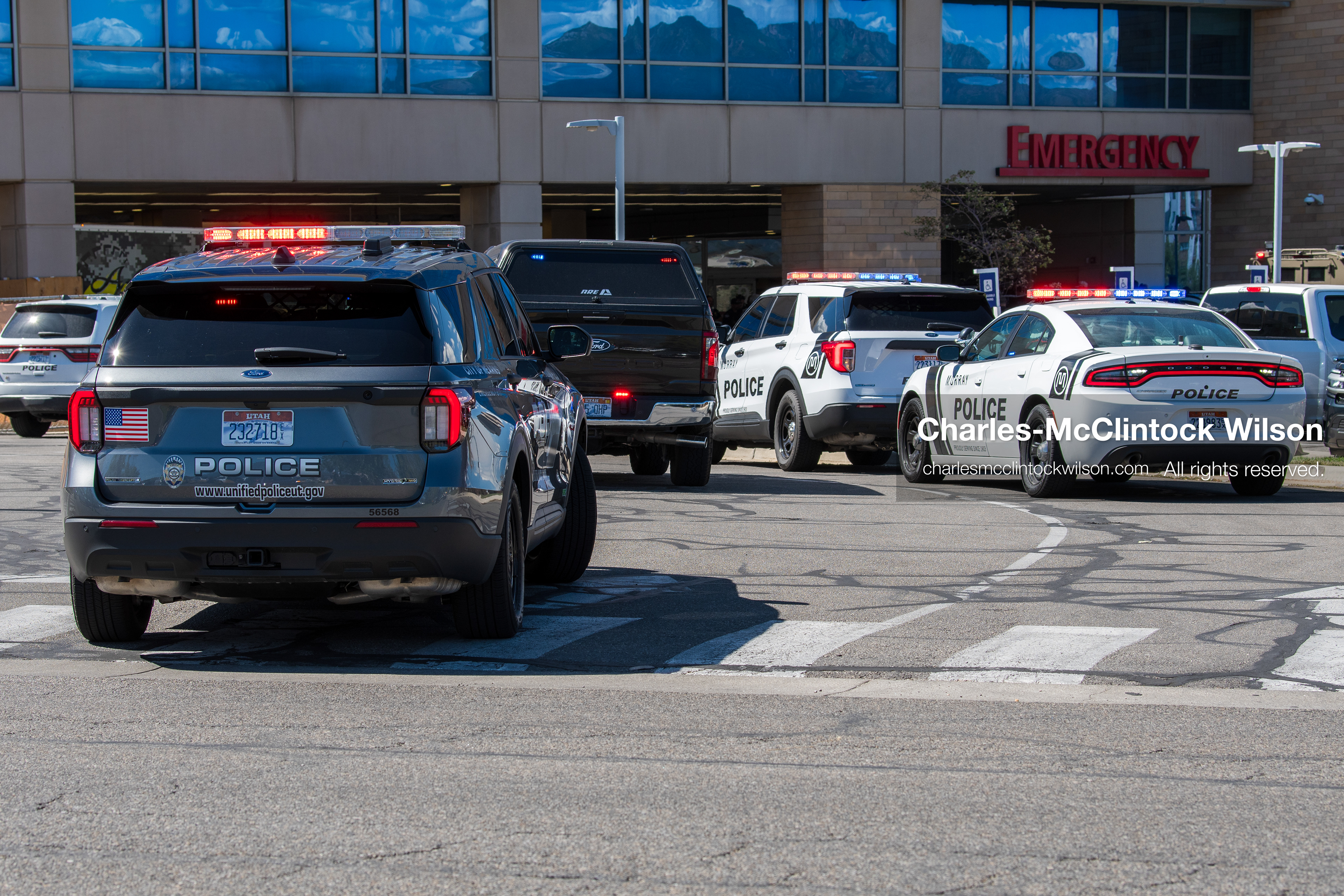 Marked police cruisers with emergency lights activated stand outside the emergency department entrance at Intermountain Medical Center in Murray, Utah, United States, on August 17, 2026. Multiple regional police agencies secured the hospital perimeter as a safety precaution after shooting victims were admitted following a fatal shootout outside a funeral service in nearby Kearns. (Photo by Charles-McClintock Wilson/NurPhoto)