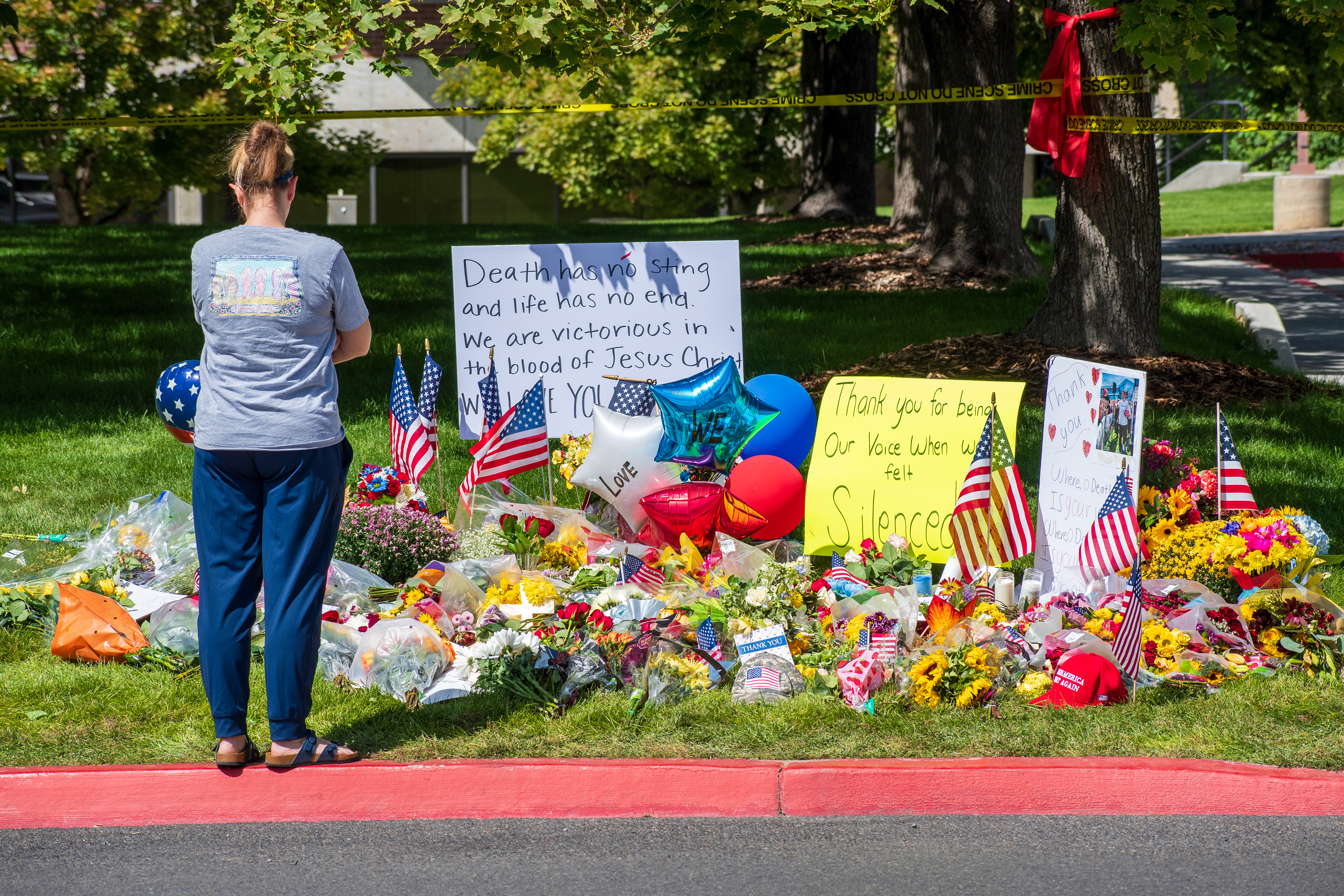 OREM, UTAH – SEPTEMBER 12, 2025: A mourner stands before a memorial site for Charlie Kirk near Utah Valley University, wearing a shirt with “LOVE” printed across the back. Flowers, American flags, balloons, and handwritten tributes line the sidewalk beneath the trees. © Charles‑McClintock Wilson / ZUMA Press