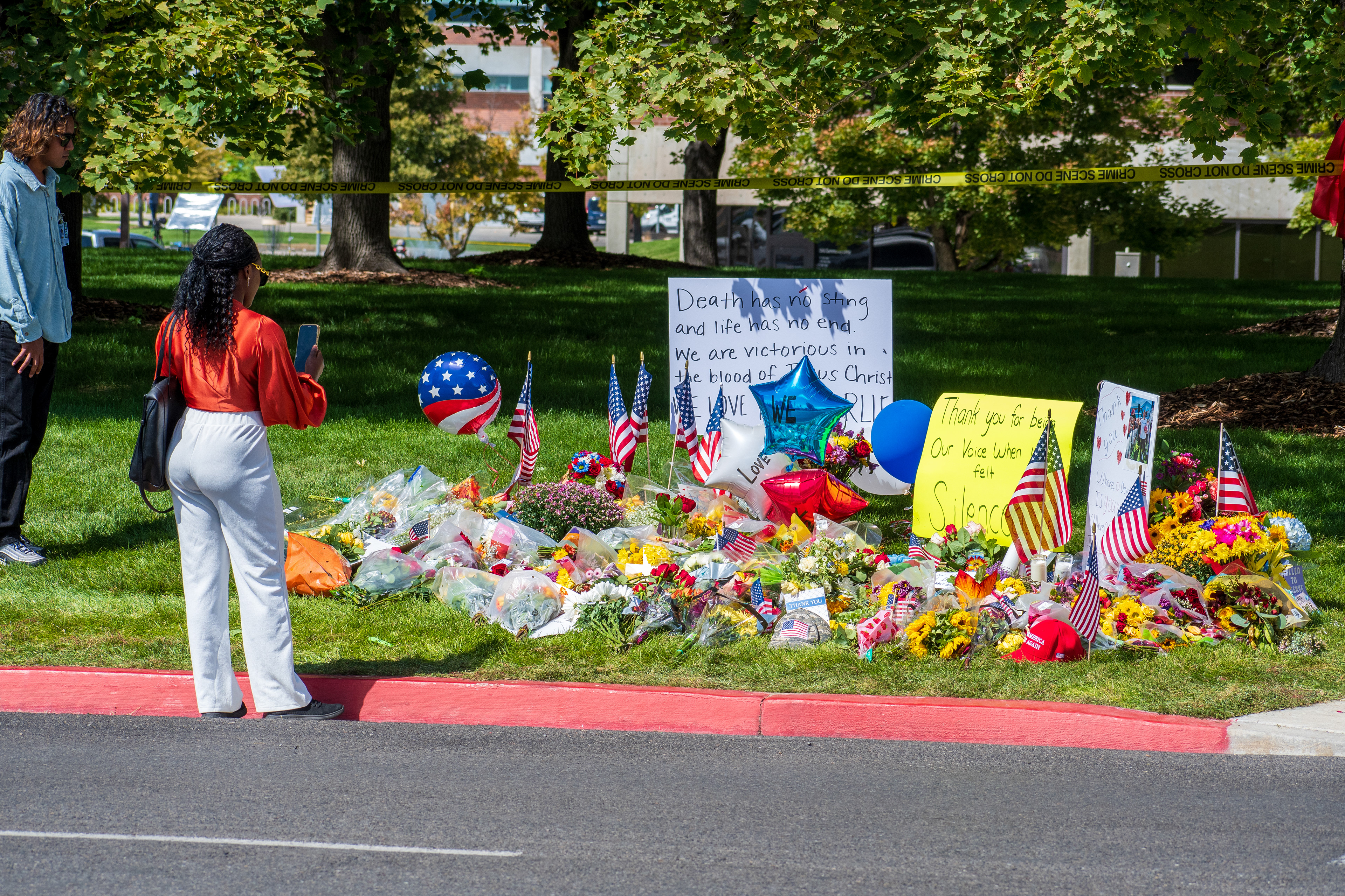 OREM, UTAH – SEPTEMBER 12, 2025: American flags, balloons, and handwritten posters are arranged beside bouquets of flowers at a memorial site for Charlie Kirk near Utah Valley University. Two mourners stand nearby as messages of gratitude and faith reflect a moment of public remembrance. © Charles‑McClintock Wilson / ZUMA Press