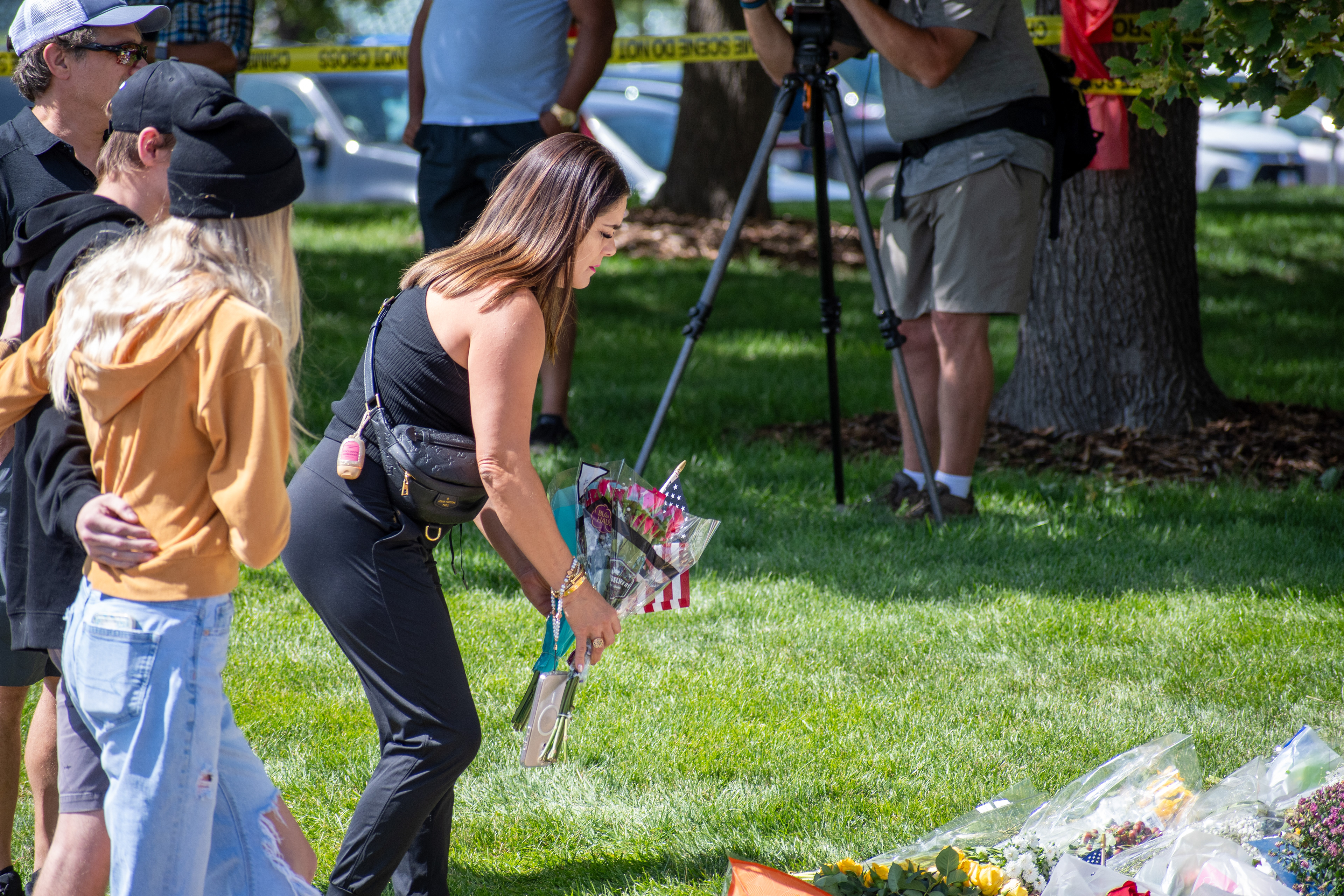 OREM, UTAH – SEPTEMBER 12, 2025: A woman kneels to arrange flowers among a growing collection of floral tributes at a memorial site for Charlie Kirk near Utah Valley University. Wrapped bouquets cover the grass as mourners gather in quiet reflection. © Charles‑McClintock Wilson / ZUMA Press