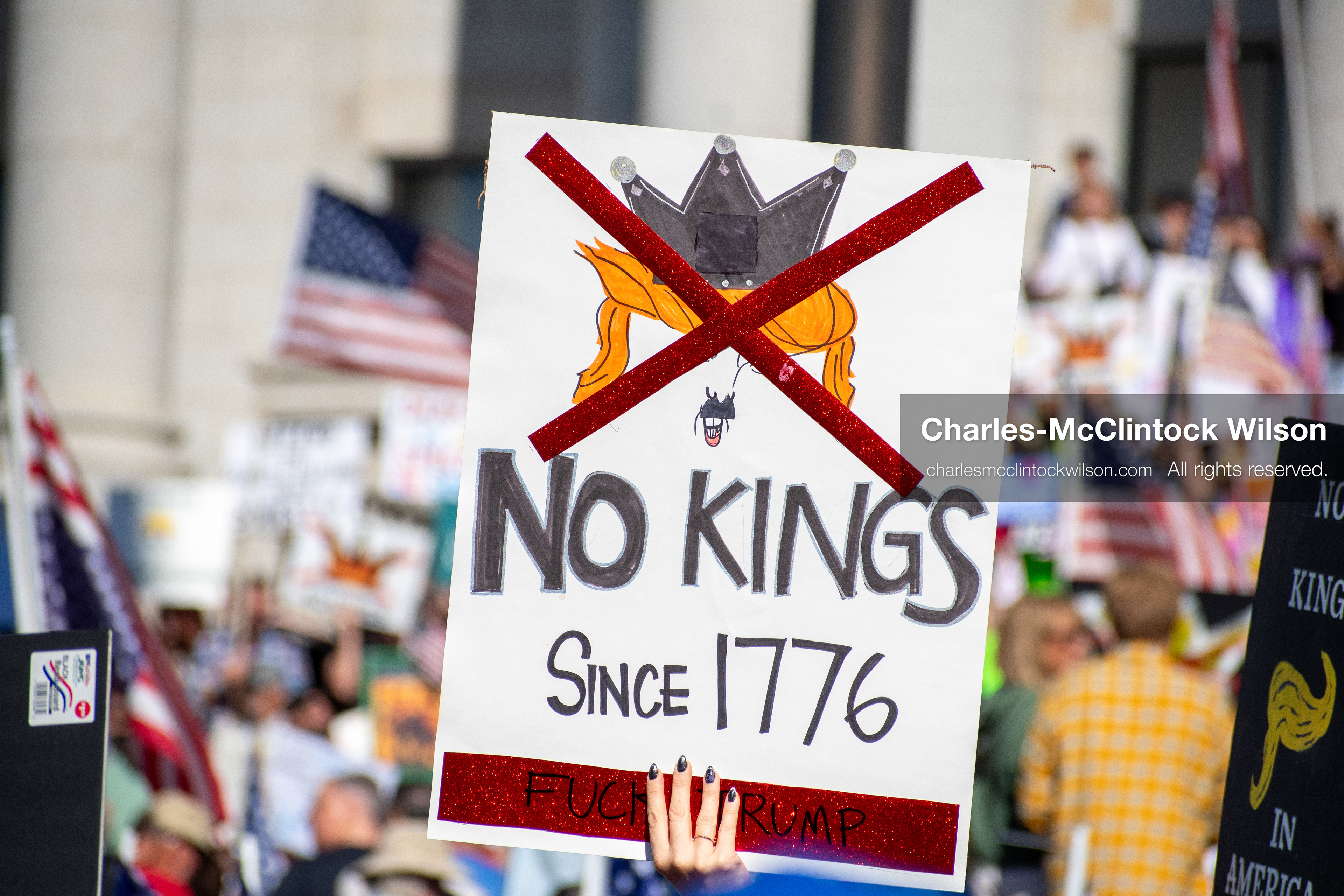 October 18, 2025, Salt Lake City, Utah, USA: A demonstrator raises a placard during a "No Kings" protest held at the Utah State Capitol. Other participants and signs are visible in the background during the public gathering.