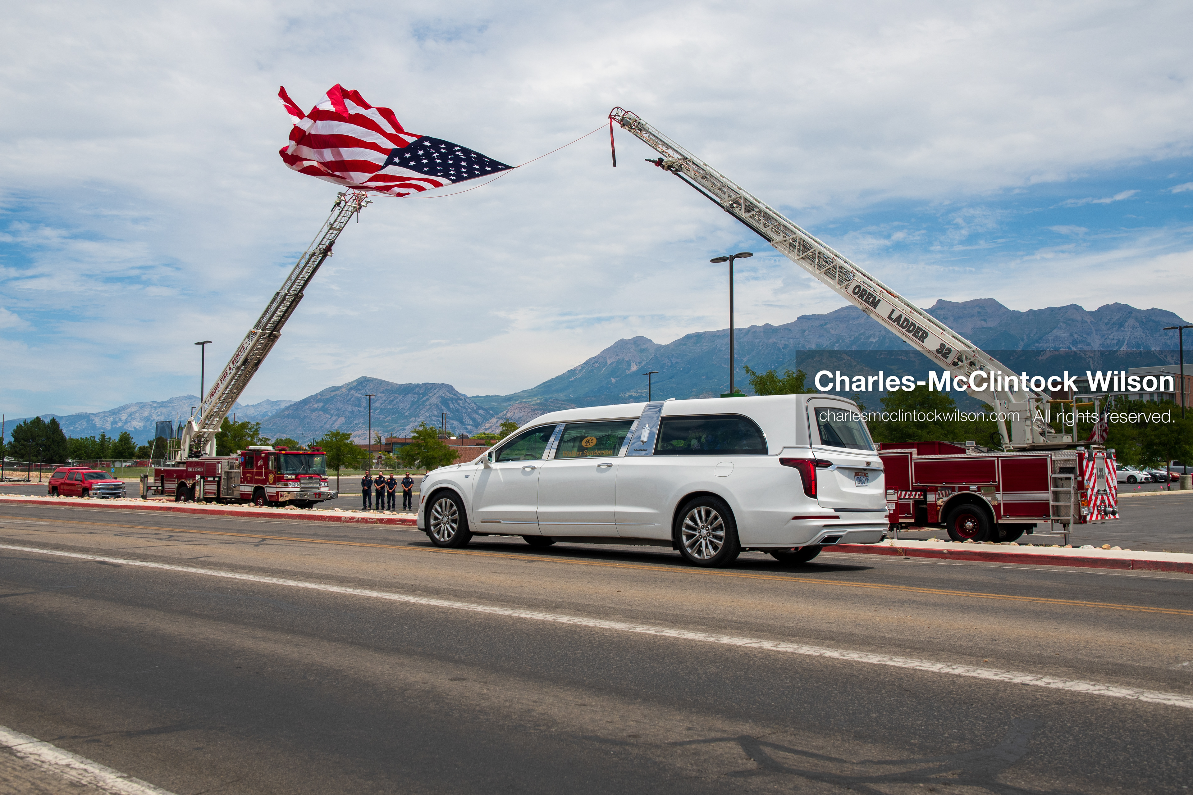 A white Cadillac hearse drives past a massive American flag suspended between two extended fire department ladder trucks during a funeral procession for Provo Fire Captain Spencer Long and his family in Orem, Utah, on Wednesday, July 29, 2026. More than 300 people came to the public memorial ceremony to honor the five family members who died after a flash flood hit their campsite near the Sunglow Campground in Wayne County. (Photo by Charles-McClintock Wilson/Sipa USA)