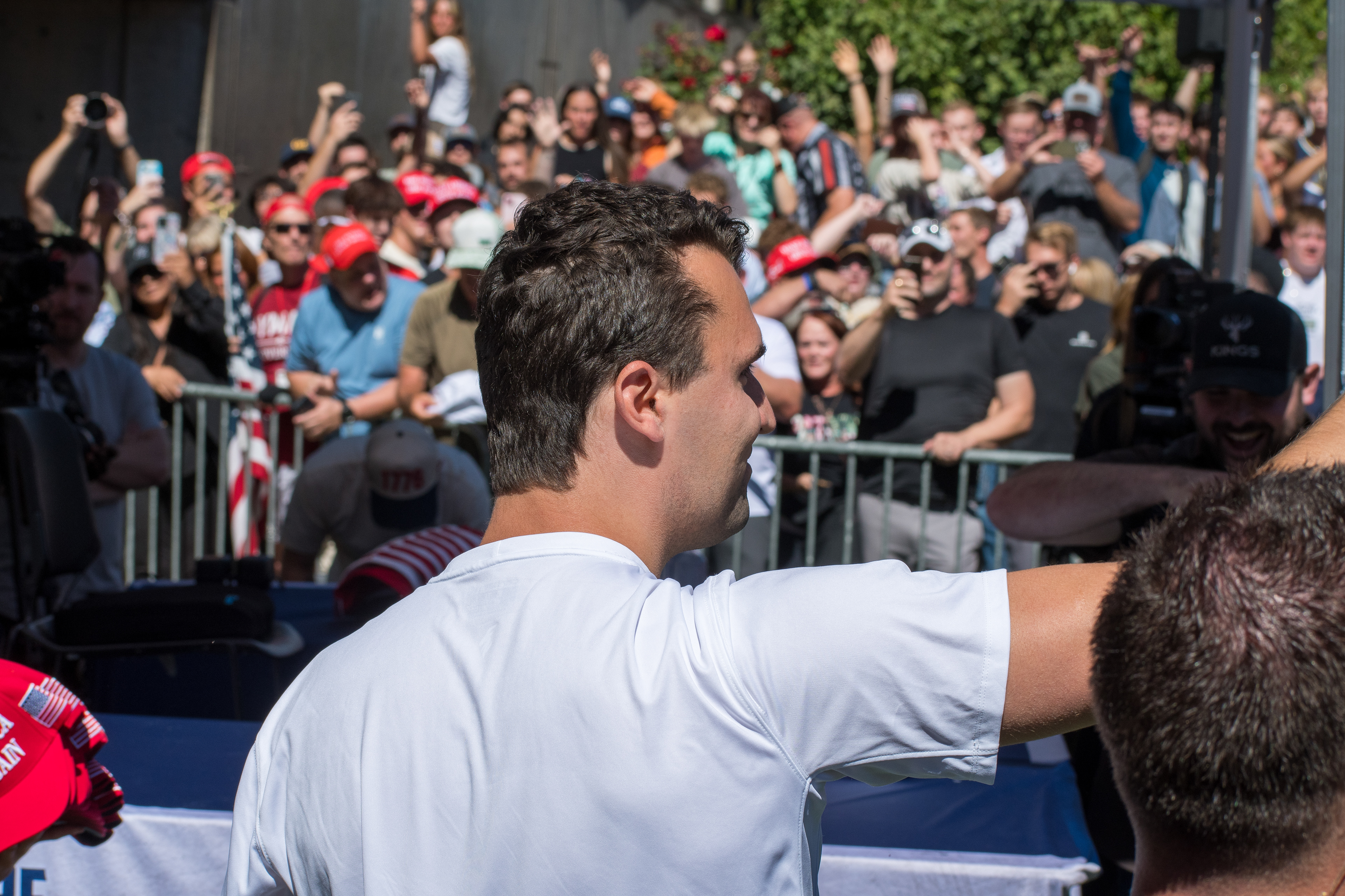 Charlie Kirk stands before a crowd of supporters during a public event at Utah Valley University. Separated by metal barricades, attendees raise phones and cheer as Kirk addresses them in one of his final public moments. The image reflects the intensity of civic engagement and the charged atmosphere that defined the gathering. © Charles-McClintock Wilson / ZUMA Press