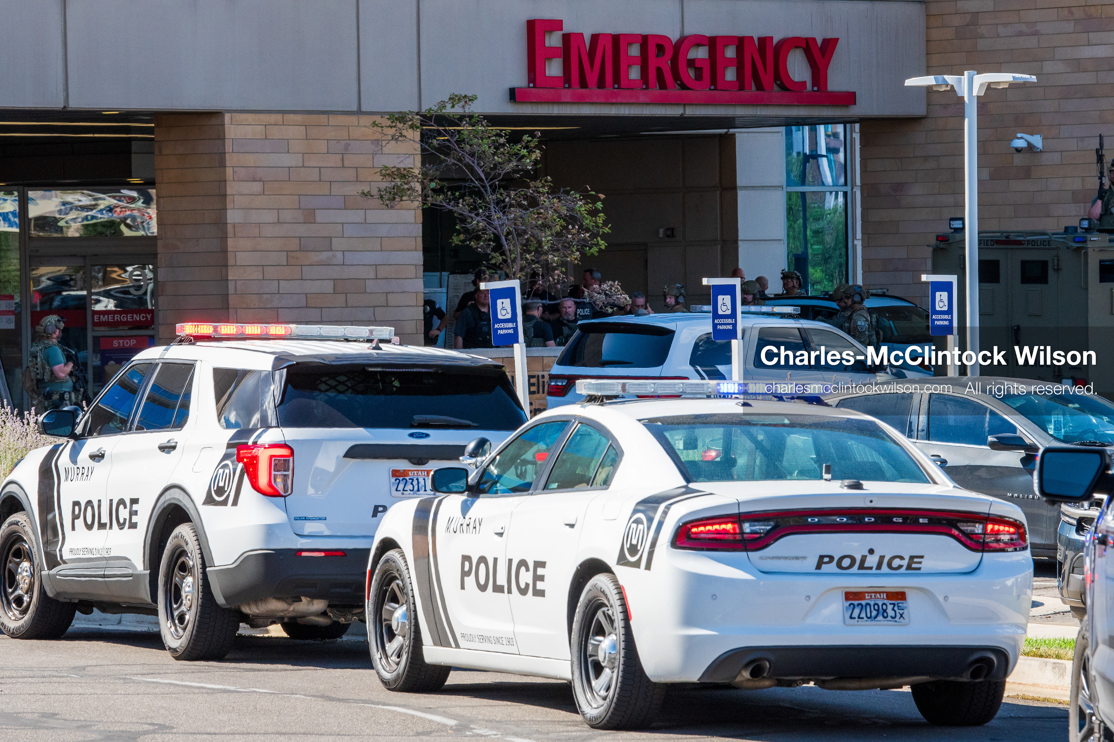 Marked police cruisers with their emergency lights flashing sit parked in a line outside the emergency room entrance at Intermountain Medical Center in Murray, Utah, United States, on August 17, 2026. Multiple regional police agencies secured the hospital perimeter as a safety precaution after shooting victims were admitted following a fatal shootout outside a funeral service in nearby Kearns. (Photo by Charles-McClintock Wilson/NurPhoto)