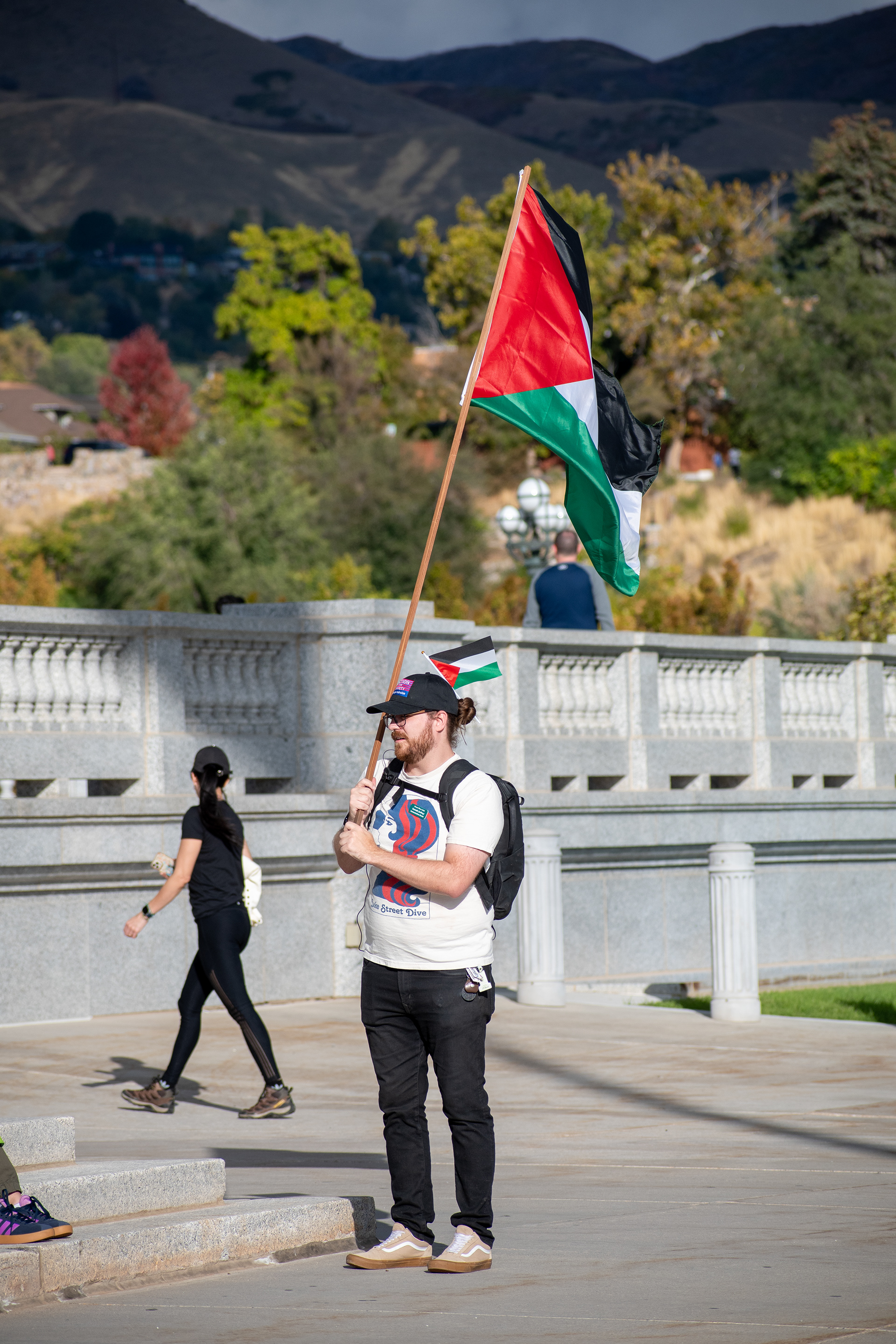 October 10, 2025, Salt Lake City, Utah, USA: A demonstrator stands with a Palestinian flag during the Free Palestine Rally organized in front of the Utah State Capitol. Mountains and stone railings frame the background as participants gather in protest. (Credit Image: © Charles-McClintock Wilson/ZUMA Press Wire)