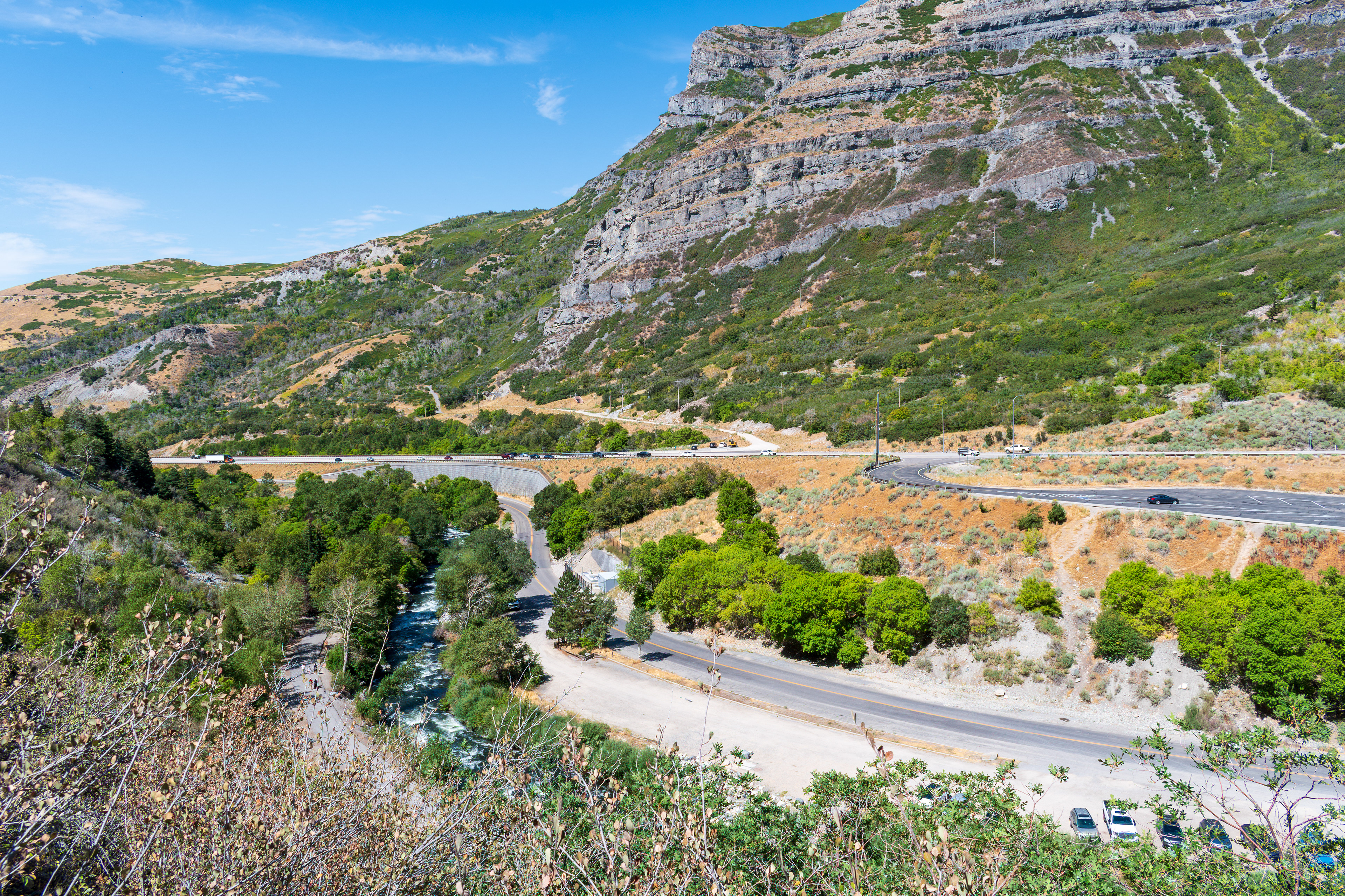 Provo, Utah, US — Sept 1, 2025: A scenic view from Bridal Veil Falls captures steep, layered rock formations and lush vegetation, with vehicles winding through the rugged terrain along U.S. Route 189.