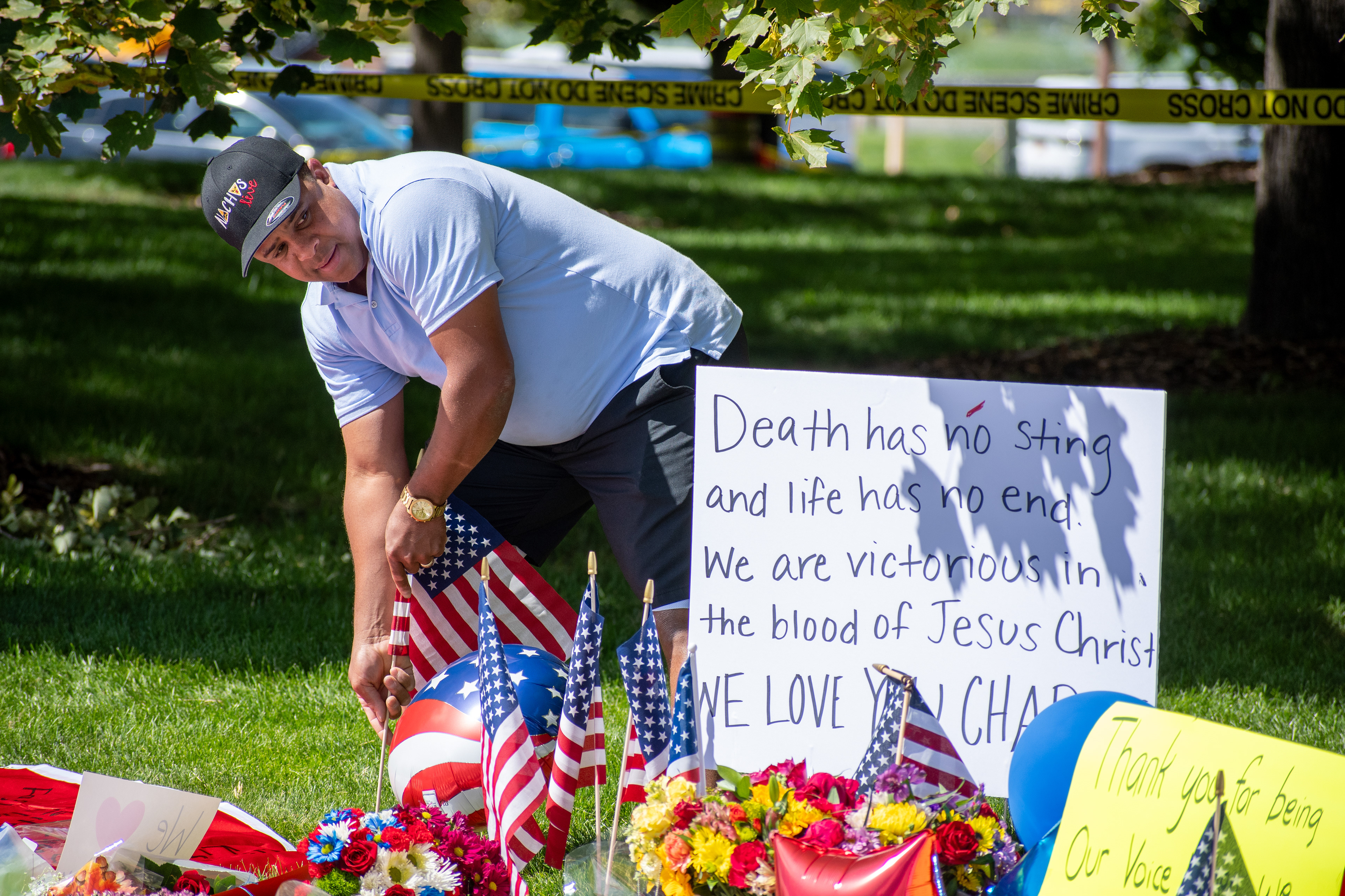 OREM, UTAH – SEPTEMBER 12, 2025: A man places American flags at a memorial site for Charlie Kirk in a shaded park near Utah Valley University. The tribute includes flowers, handwritten posters, and personal items arranged beneath the trees. © Charles‑McClintock Wilson / ZUMA Press