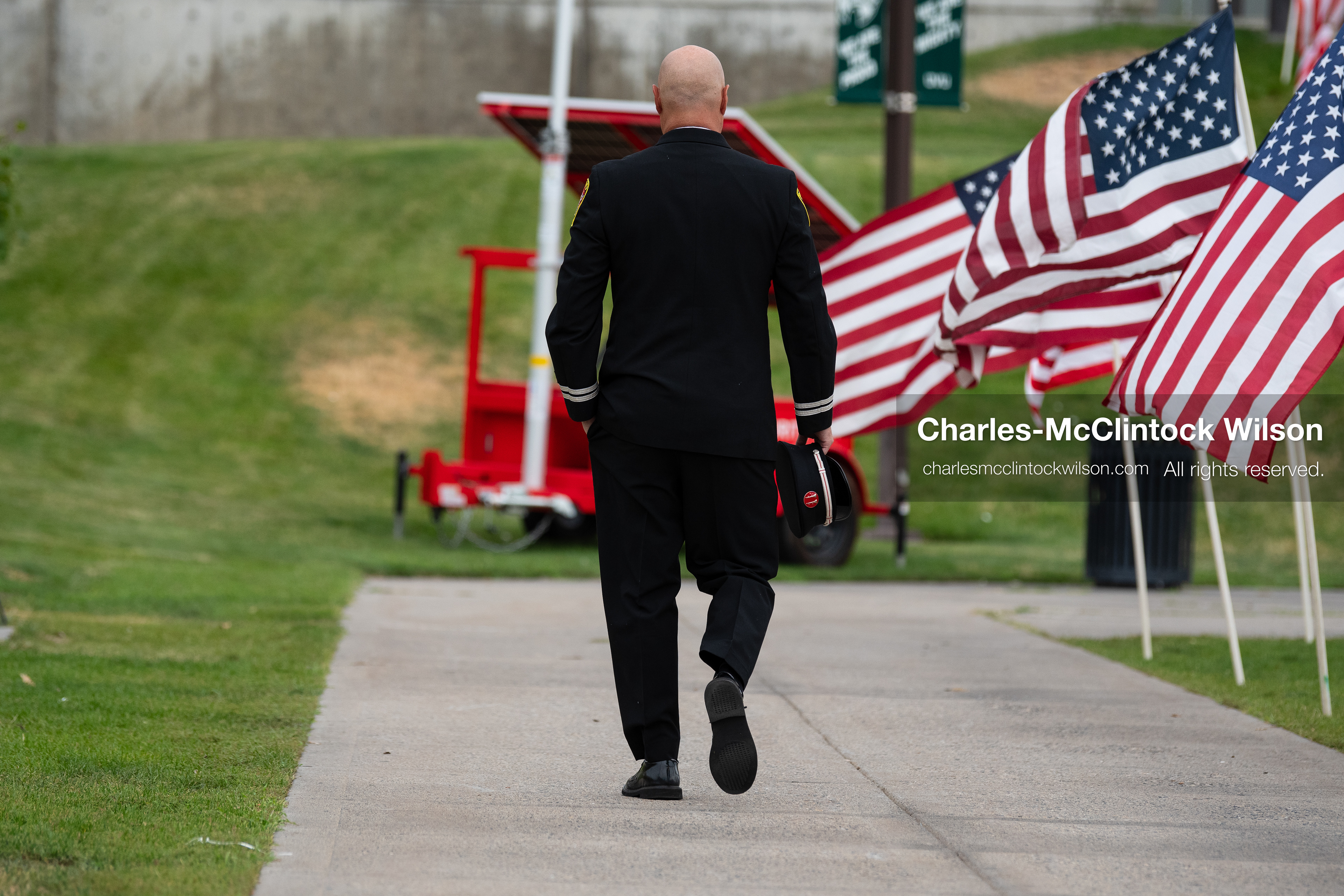 A first responder walks away down a concrete sidewalk lined with American flags outside the UCCU Center at Utah Valley University in Orem, Utah, on Wednesday, July 29, 2026. More than 300 people came to the public memorial ceremony to honor Provo Fire Captain Spencer Long, his wife Katrina, and three of their sons, who died after a flash flood hit their campsite near the Sunglow Campground in Wayne County. (Photo by Charles-McClintock Wilson/Sipa USA)