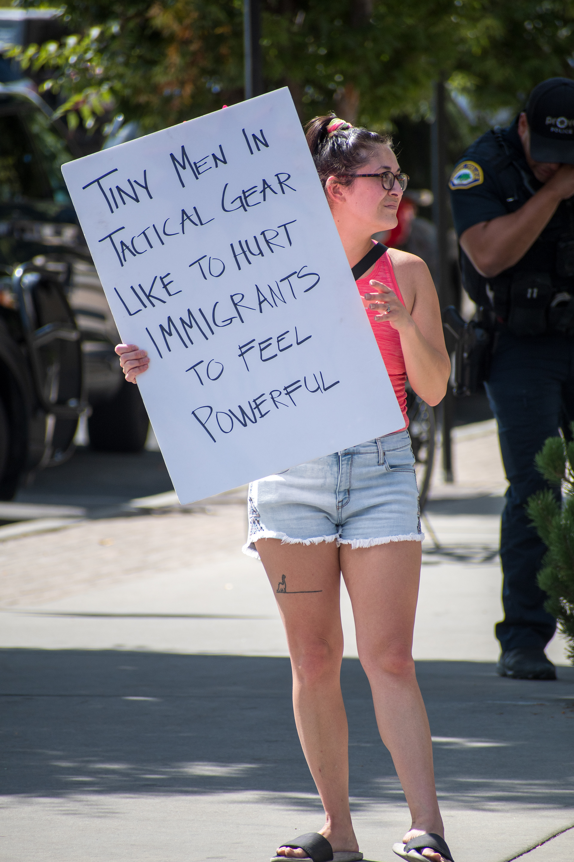 September 15, 2025 – Provo, Utah, United States: A demonstrator holds a sign reading “Tiny Men In Tactical Gear Like To Hurt IMMIGRANTS To Feel Powerful” outside the Utah Valley Convention Center during a protest against the Department of Homeland Security career expo. A police officer in tactical gear stands nearby as protestors voice opposition to federal enforcement practices. Photograph by Charles‑McClintock Wilson / ZUMA Press Wire
