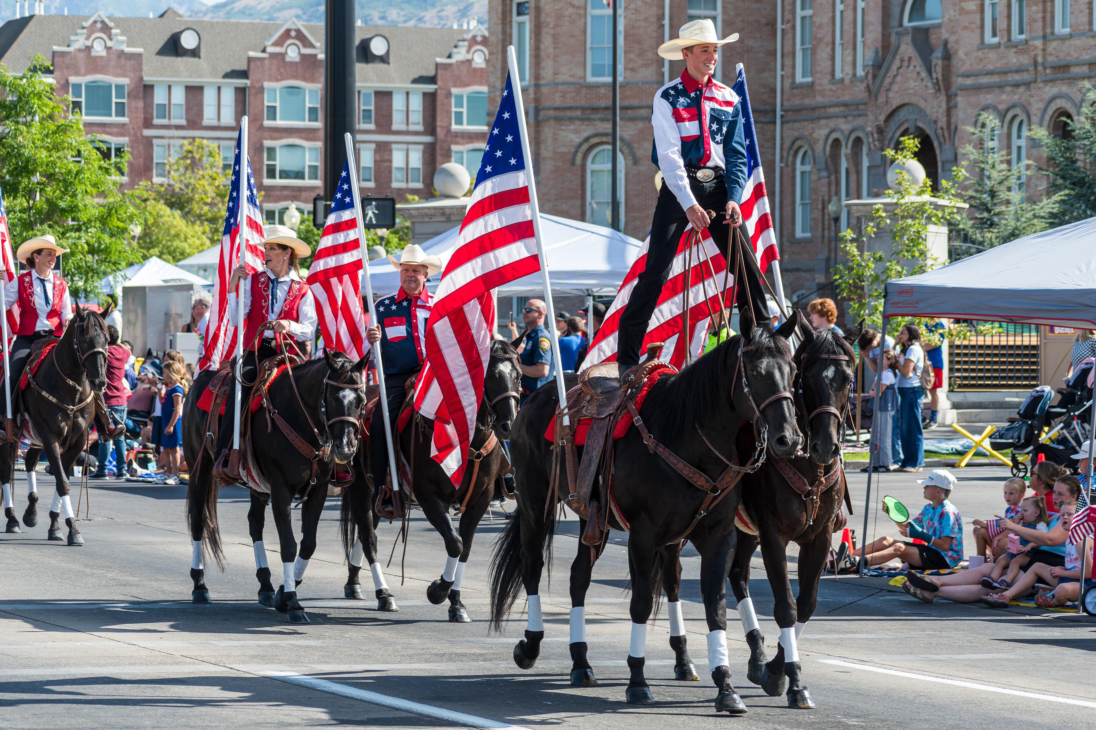 Provo, Utah – July 4, 2025: Western equestrian riders carry U.S. flags during the Freedom Festival Grand Parade. One rider stands atop two horses, thrilling spectators on University Avenue.