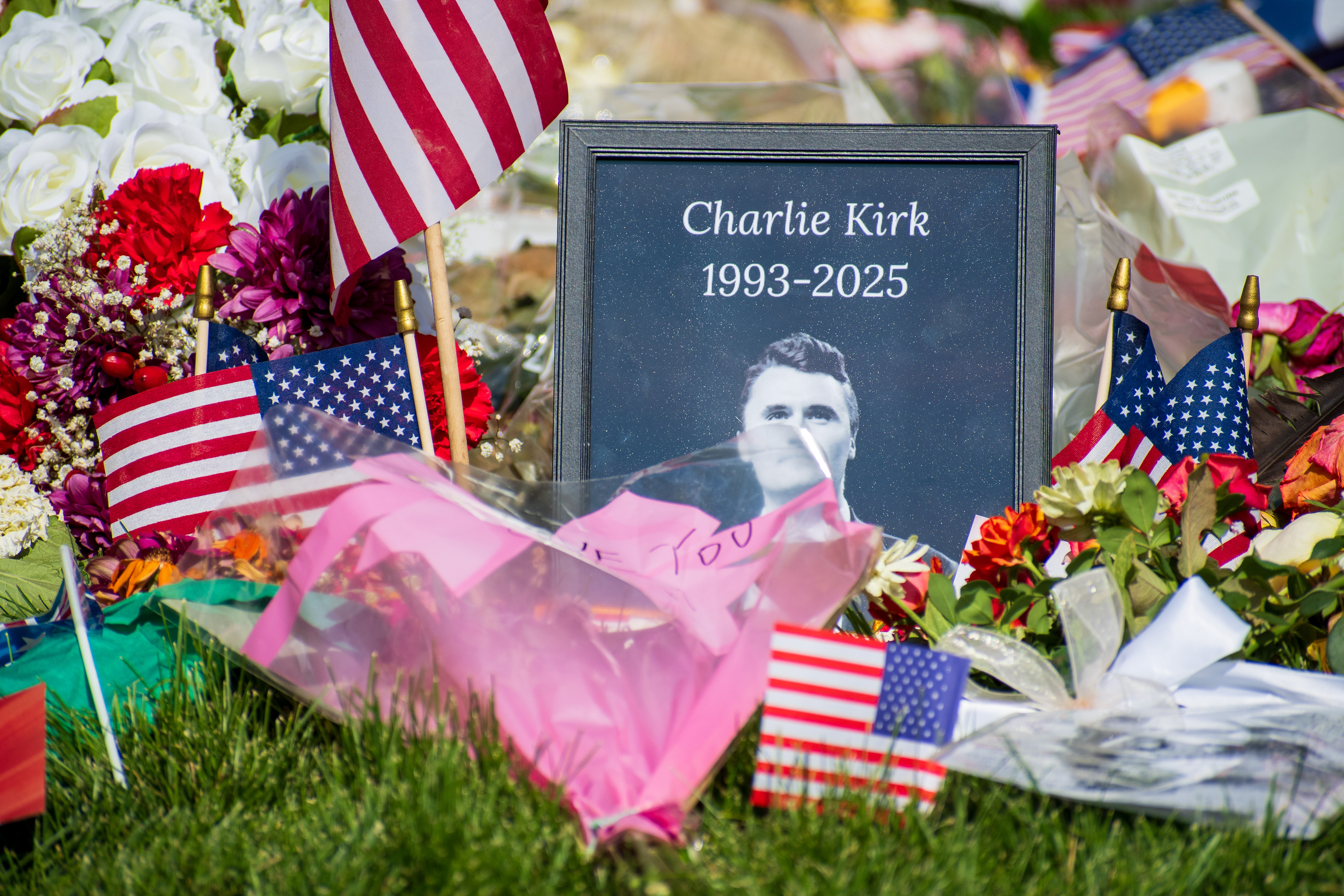 OREM, UTAH – SEPTEMBER 15, 2025: A framed photograph labeled “Charlie Kirk 1993–2025” is displayed at a memorial site on the campus of Utah Valley University. American flags, flowers, and tribute items are arranged on the grass surrounding the portrait. © Charles‑McClintock Wilson / ZUMA Press