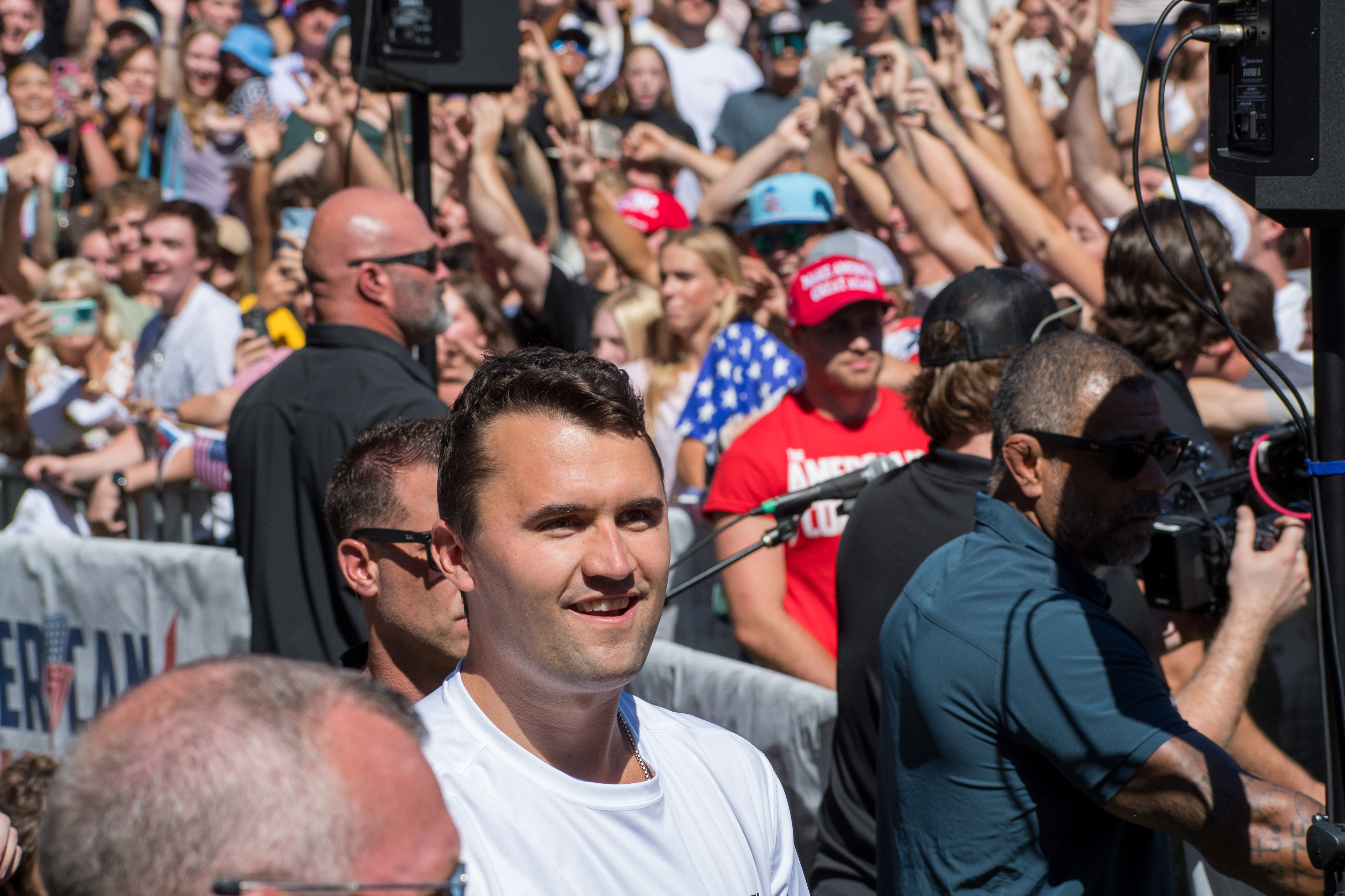 Charlie Kirk stands before a crowd of supporters during a public event at Utah Valley University. Separated by metal barricades, attendees raise phones and cheer as Kirk addresses them in one of his final public moments. The image reflects the intensity of civic engagement and the charged atmosphere that defined the gathering. © Charles-McClintock Wilson / ZUMA Press