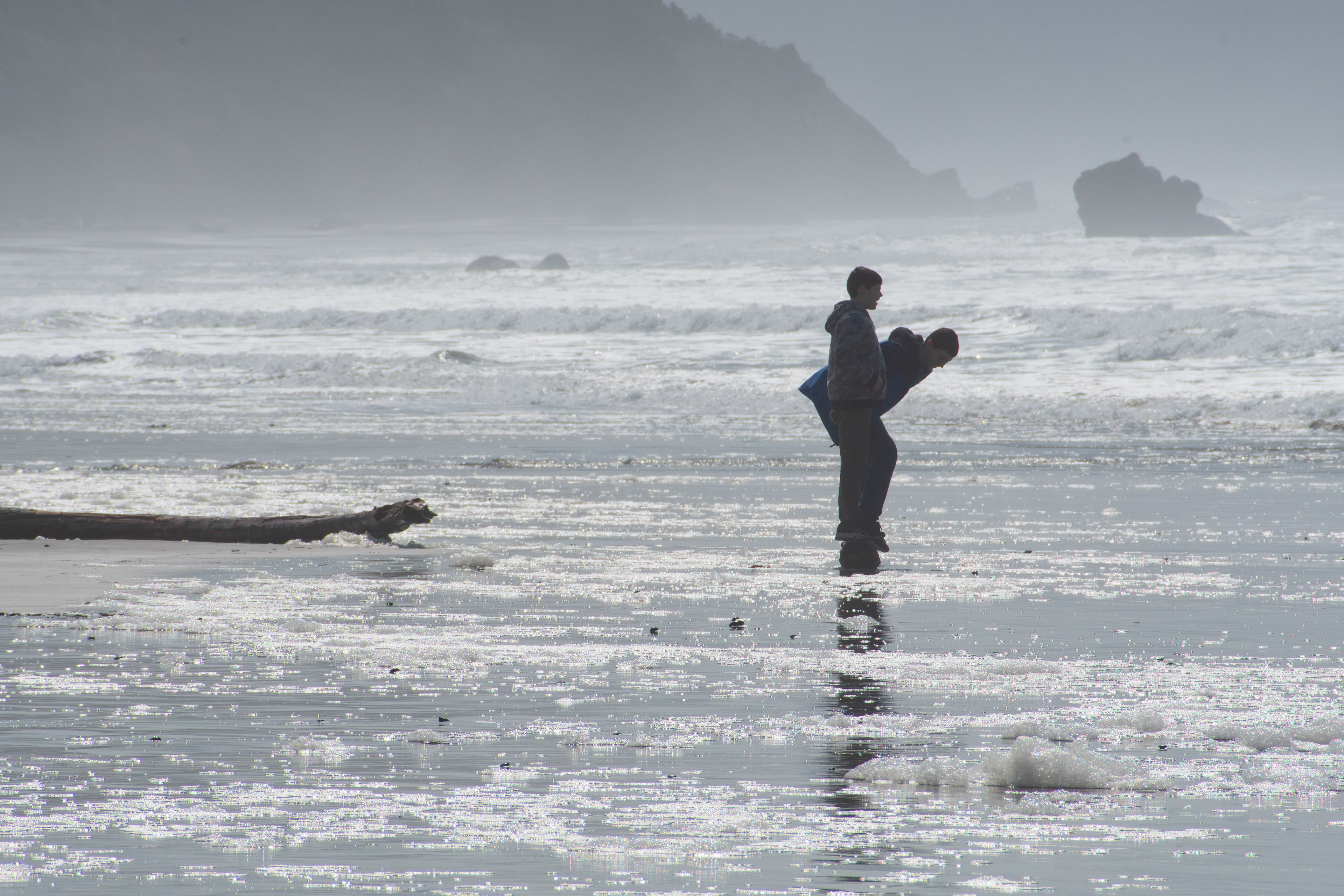 CANNON BEACH, OR - APRIL 12: Two boys play along the shoreline as waves roll in at Cannon Beach on April 12, 2025, in Cannon Beach, Oregon. The beach is known for its dramatic coastal landscape, including Haystack Rock, and draws families and tourists year-round. 