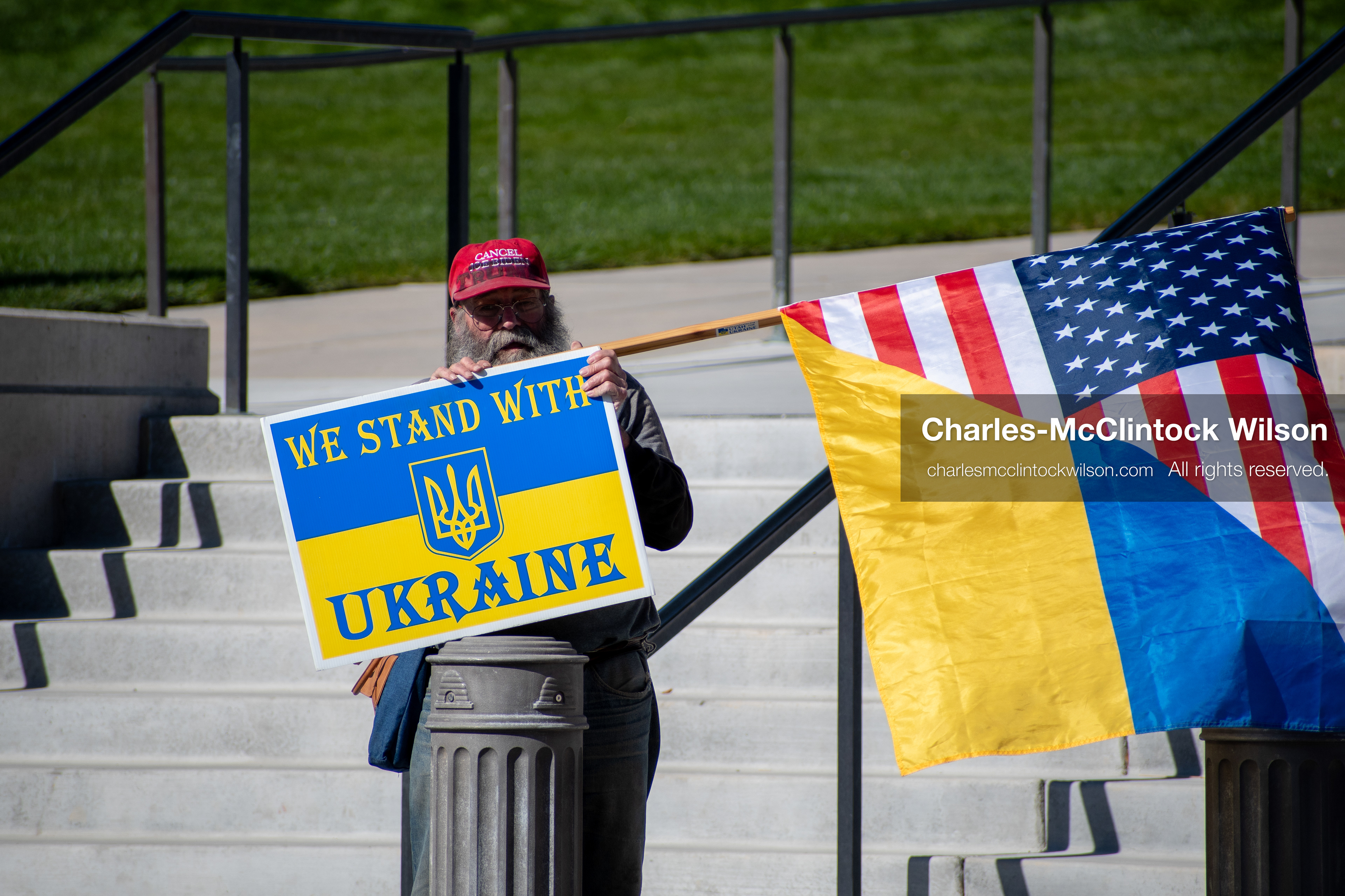 October 18, 2025, Salt Lake City, Utah, USA: A demonstrator stands with American and Ukrainian flags and a sign reading "We Stand With Ukraine" during a public protest at the Utah State Capitol in Salt Lake City, Utah. The protest was part of a nationwide mobilization.