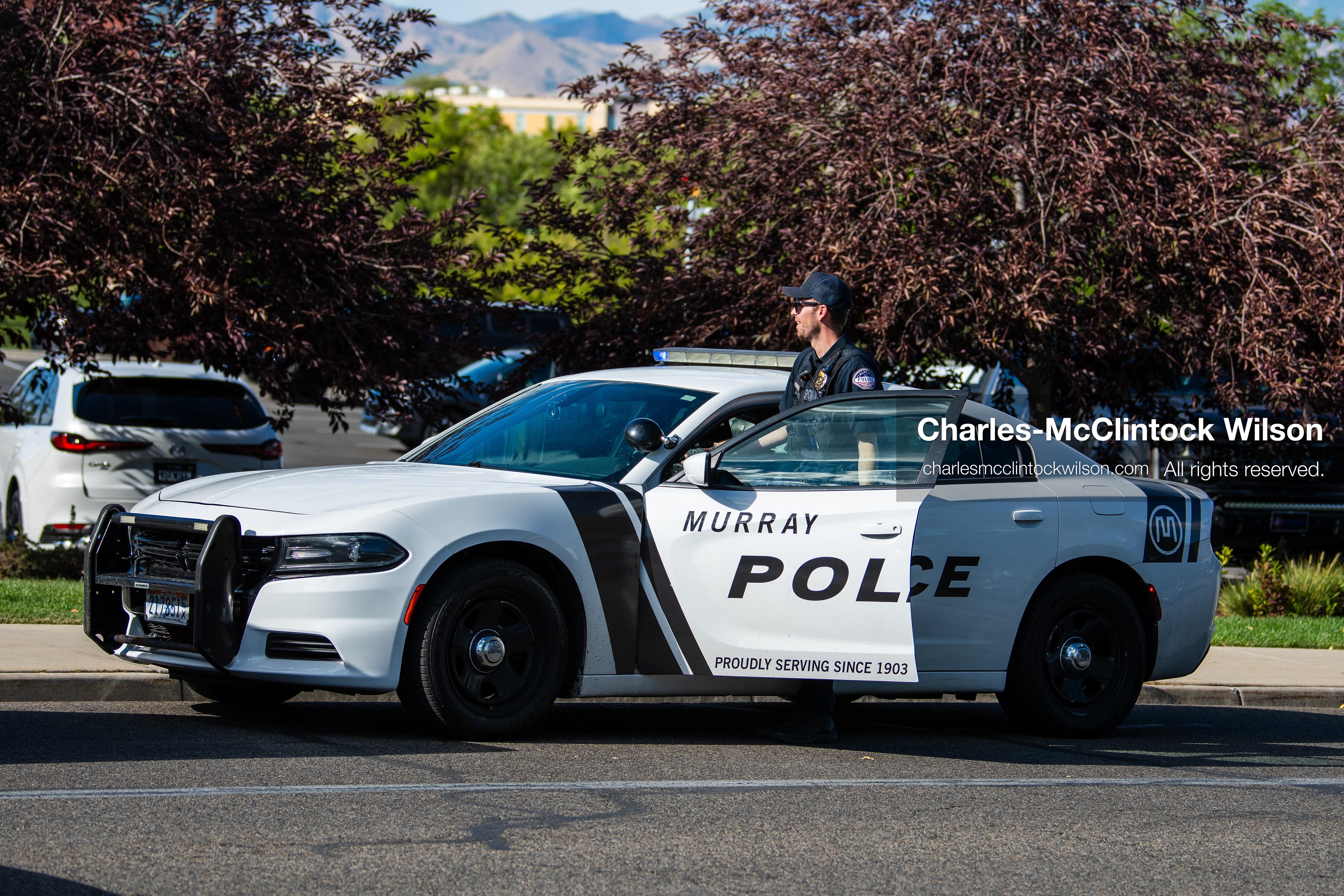 A Murray City Police officer stands behind the open driver-side door of a marked police cruiser parked outside Intermountain Medical Center in Murray, Utah, United States, on August 17, 2026. Multiple regional police agencies secured the hospital perimeter as a safety precaution after shooting victims were admitted following a fatal shootout outside a funeral service in nearby Kearns. (Photo by Charles-McClintock Wilson/NurPhoto)