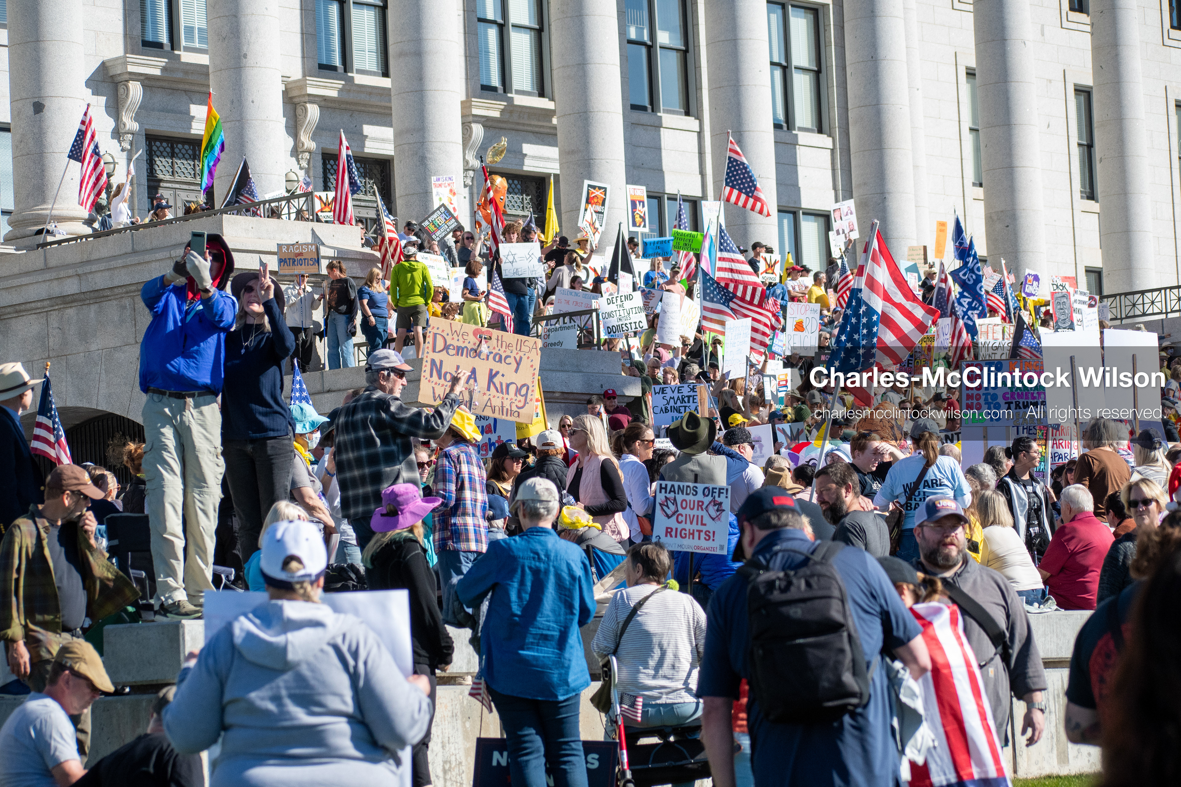 October 18, 2025, Salt Lake City, Utah, USA: Demonstrators gather on the steps of the Utah State Capitol during a "No Kings" protest held as part of a nationwide mobilization. Participants hold signs and flags while documenting the event. The protest was one of several organized across the United States.