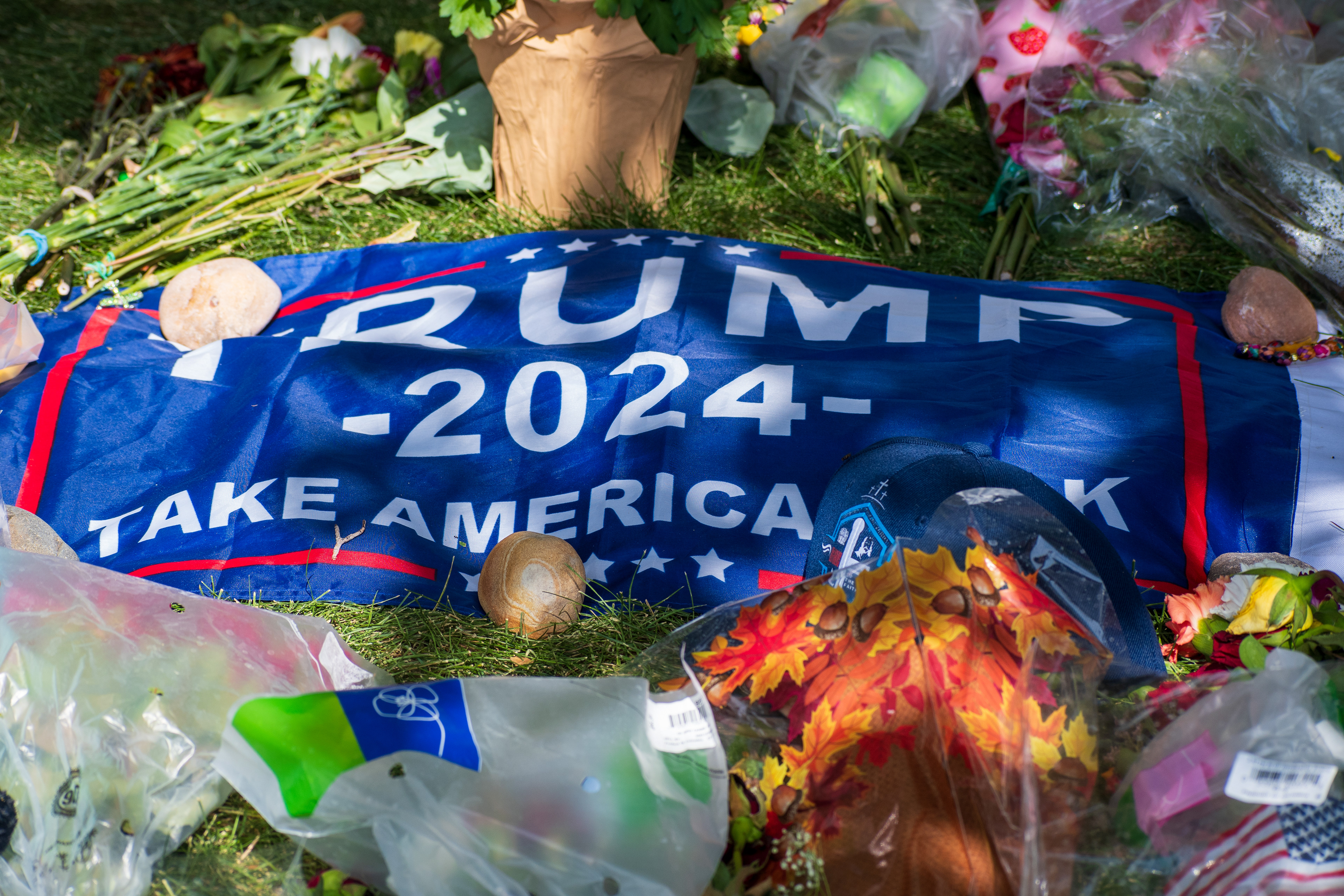 OREM, UTAH – SEPTEMBER 15, 2025: A “TRUMP 2024 TAKE AMERICA BACK” banner is displayed at a memorial site for Charlie Kirk on the campus of Utah Valley University. Flowers, candles, plastic bags, and a pumpkin with a sunflower decoration are arranged around the banner. © Charles‑McClintock Wilson / ZUMA Press