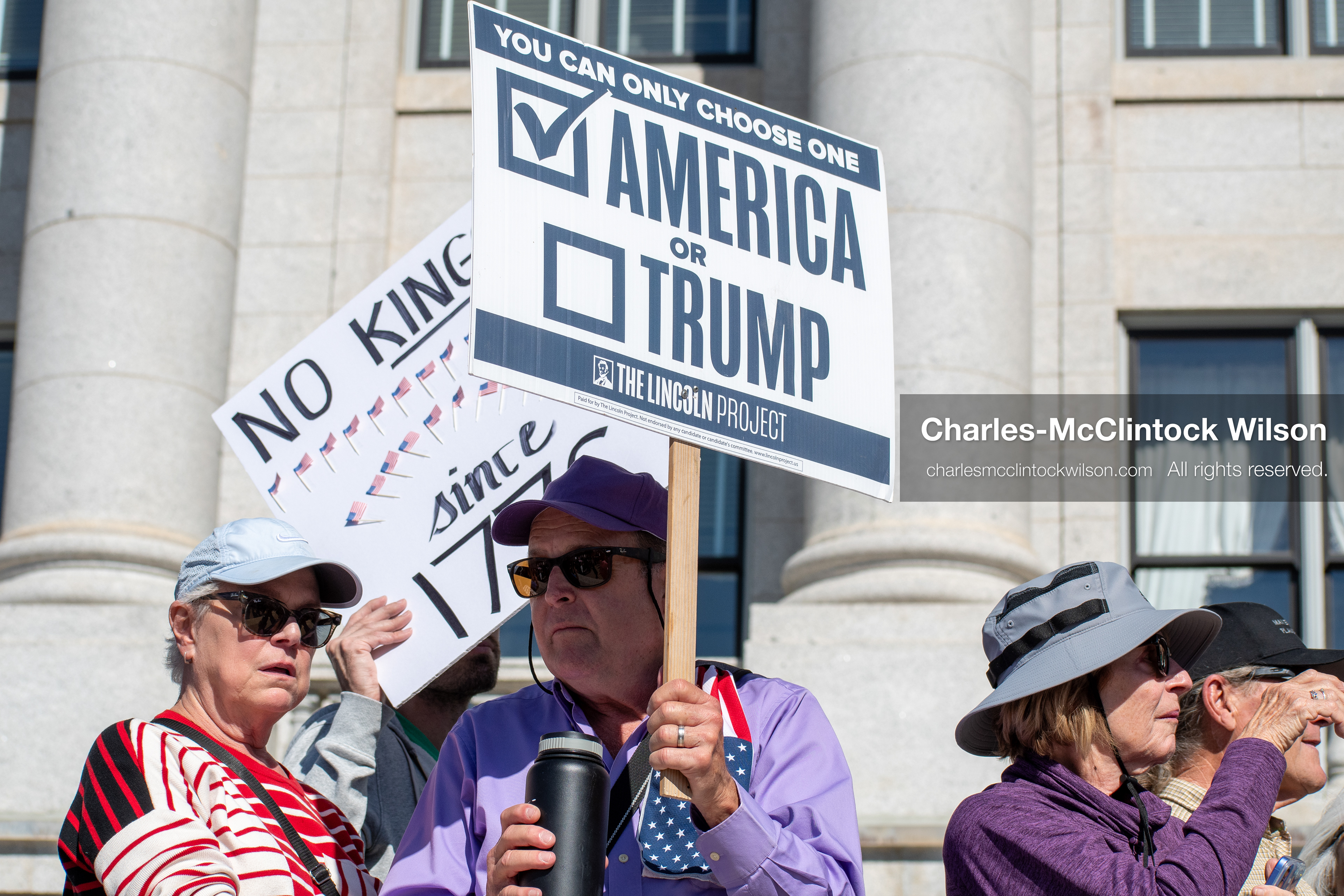 October 18, 2025, Salt Lake City, Utah, USA: A demonstrator raises a placard during a "No Kings" protest held at the Utah State Capitol. Other participants and signs are visible in the background during the public gathering.