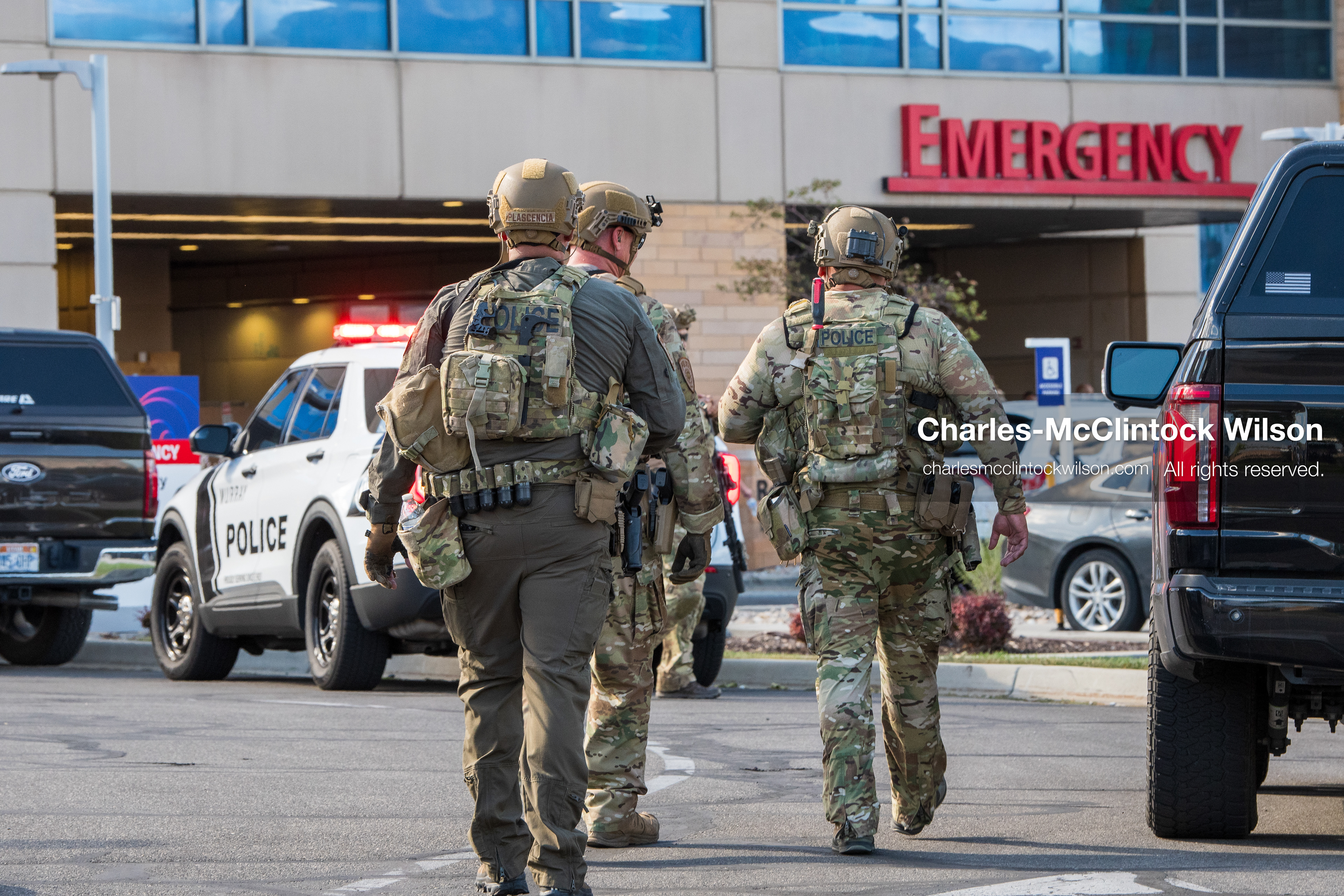 Three armed law enforcement officers in full tactical gear and helmets patrol the parking area near the emergency department entrance at Intermountain Medical Center in Murray, Utah, United States, on August 17, 2026. Multiple regional police agencies secured the hospital perimeter as a safety precaution after shooting victims were admitted following a fatal shootout outside a funeral service in nearby Kearns. (Photo by Charles-McClintock Wilson/NurPhoto)