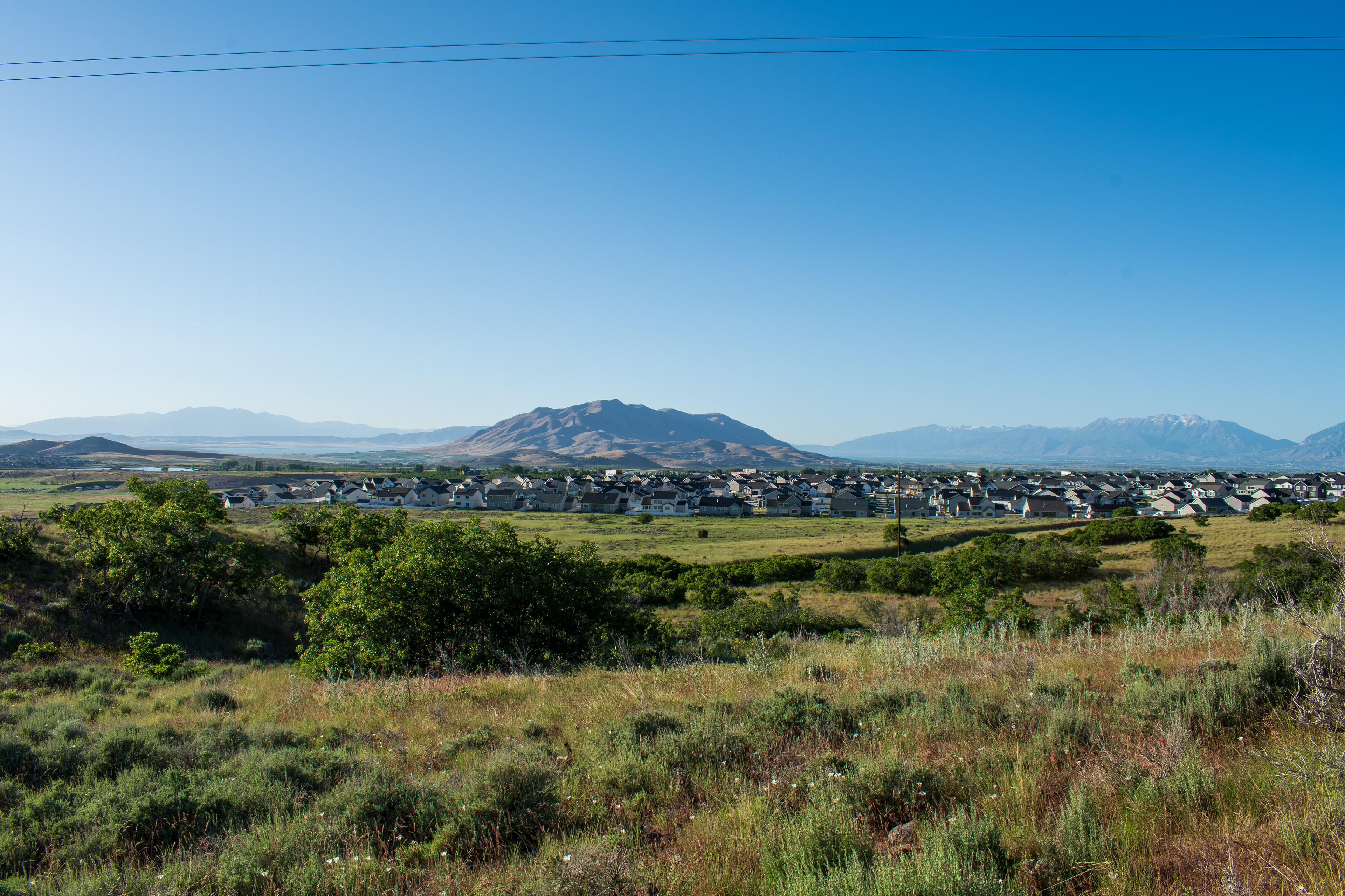 Santaquin, Utah – June 2, 2025: Wide view of a residential neighborhood with a mountainous backdrop and open valley under a clear sky.