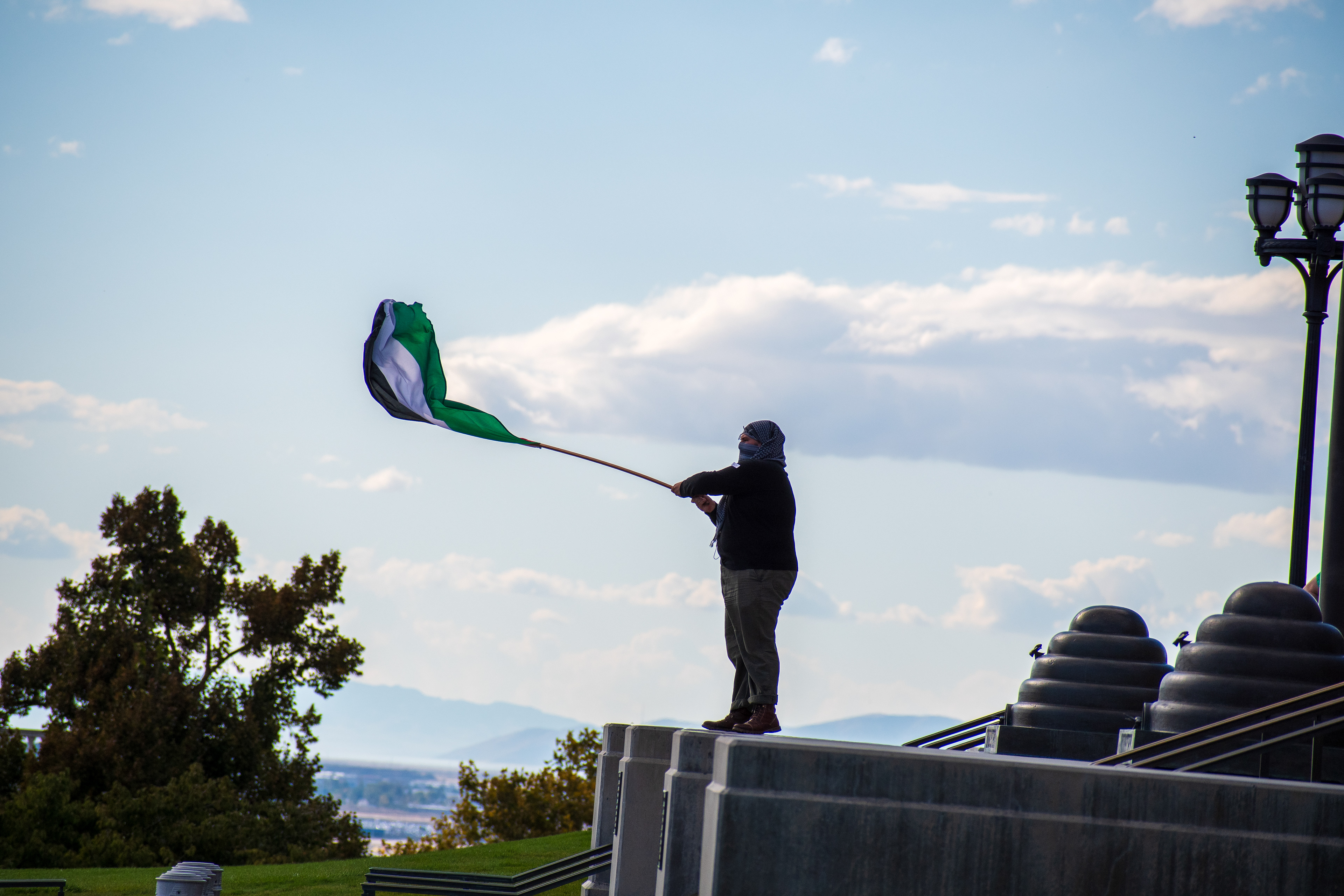 October 10, 2025, Salt Lake City, Utah, USA: A demonstrator stands on a raised platform outside the Utah State Capitol during the Free Palestine Rally. The participant waves a Palestinian flag while wearing a face covering and casual clothing. (Credit Image: © Charles-McClintock Wilson/ZUMA Press Wire)