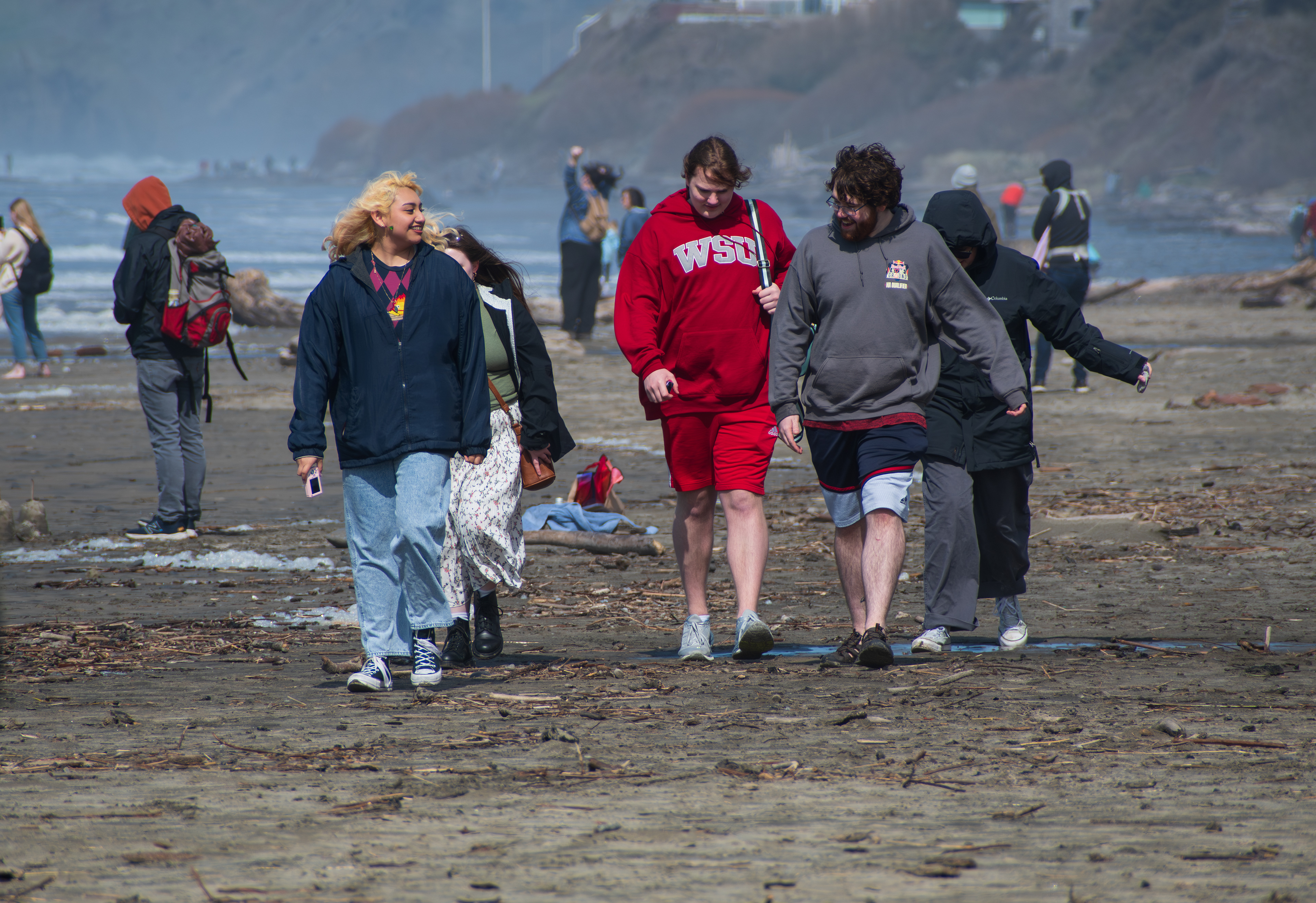 CANNON BEACH, OR, USA - APR 12, 2025: Visitors walk along the sandy shores of Cannon Beach under a cloudy sky, with the iconic Haystack Rock standing tall against the backdrop of the Pacific Ocean