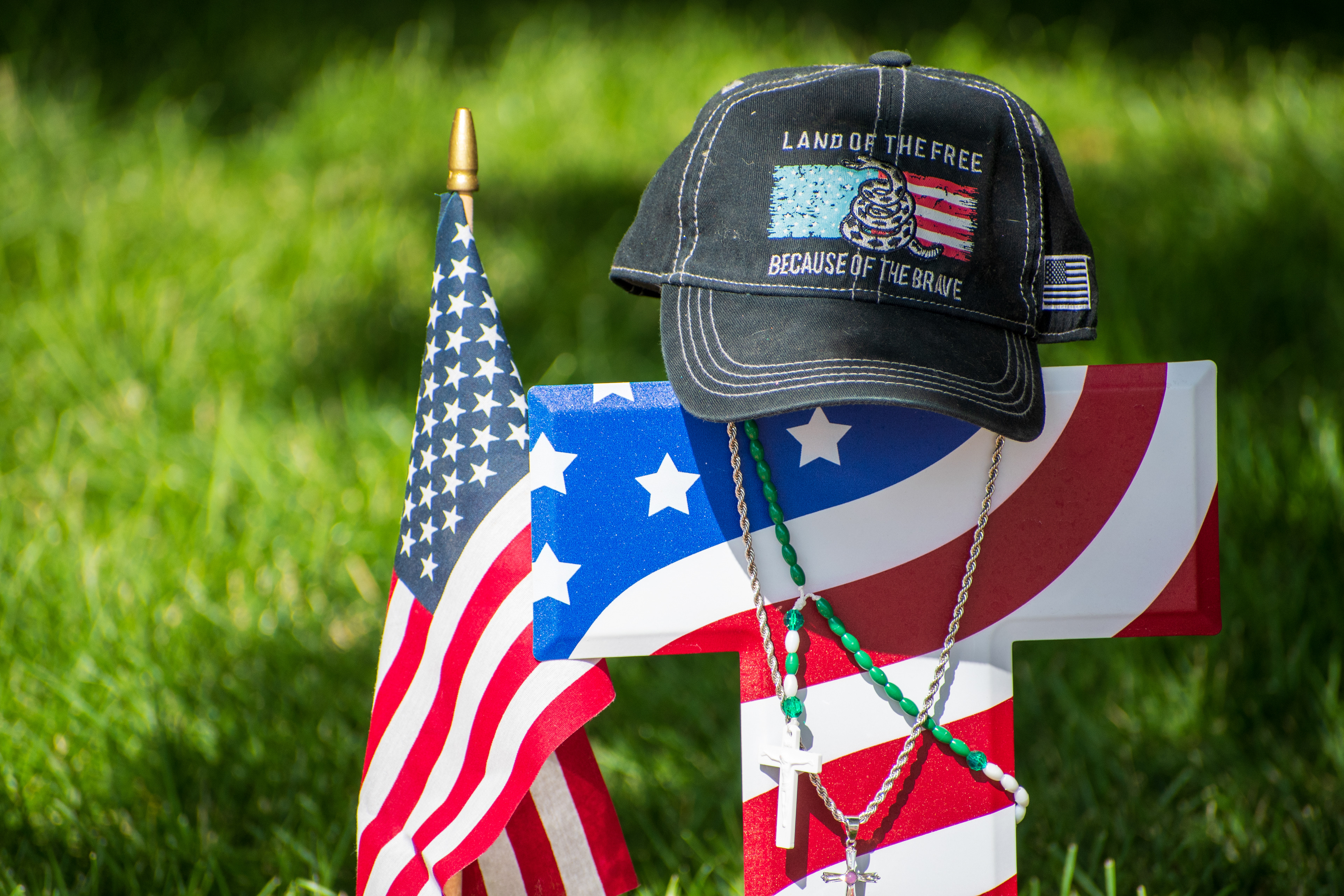 OREM, UTAH – SEPTEMBER 15, 2025: A cross wrapped in an American flag design is seen at a memorial honoring Charlie Kirk on the campus of Utah Valley University. A black baseball cap reading “LAND OF THE FREE BECAUSE OF THE BRAVE” rests atop the cross, alongside a small flag and a silver necklace with a cross pendant. © Charles‑McClintock Wilson / ZUMA Press