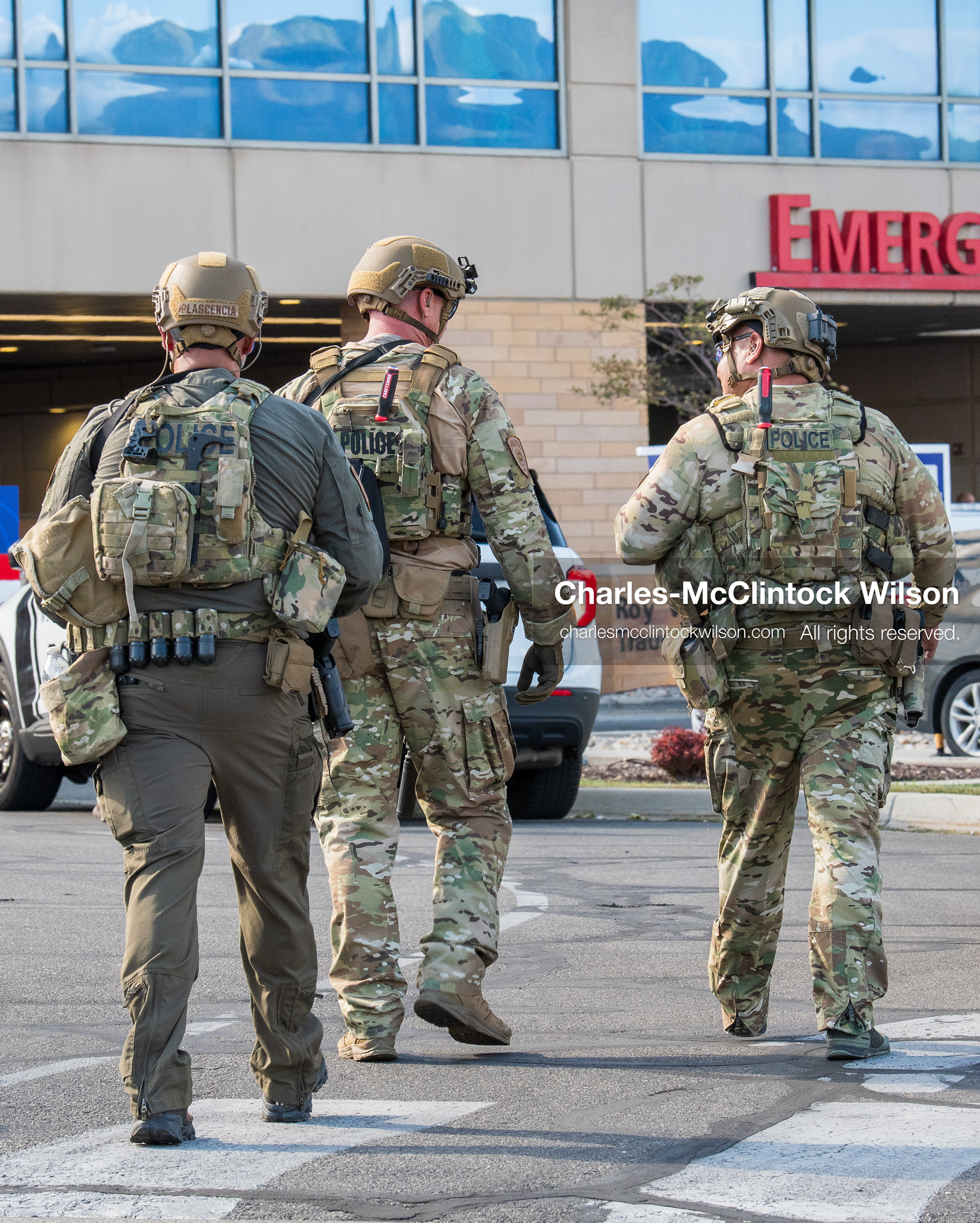 Three armed law enforcement officers in full tactical gear and helmets patrol the parking area near the emergency department entrance at Intermountain Medical Center in Murray, Utah, United States, on August 17, 2026. Multiple regional police agencies secured the hospital perimeter as a safety precaution after shooting victims were admitted following a fatal shootout outside a funeral service in nearby Kearns. (Photo by Charles-McClintock Wilson/NurPhoto)