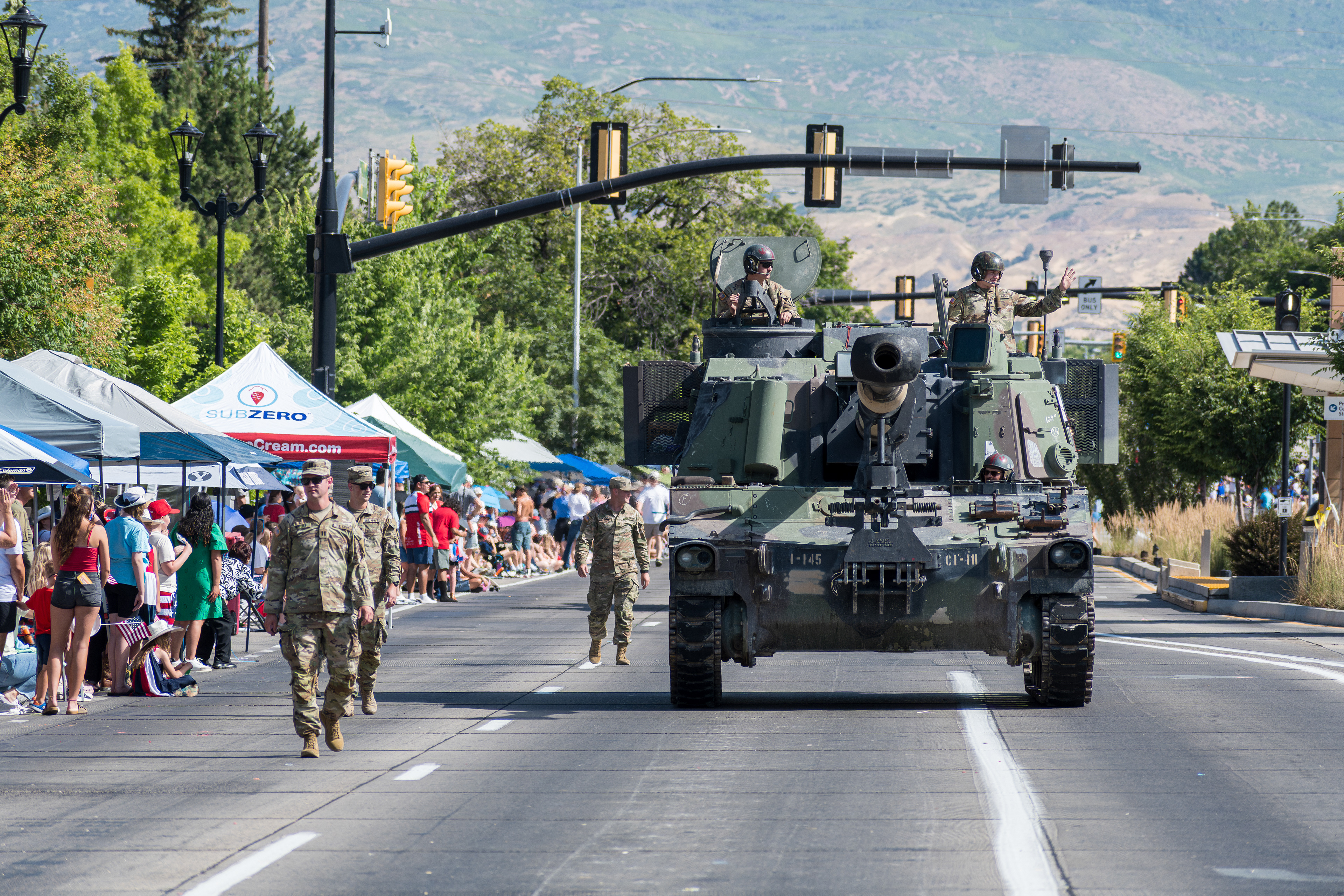 Provo, Utah – July 4, 2025: U.S. Army personnel ride atop a tank as others march beside it during the Freedom Festival Grand Parade in downtown Provo.