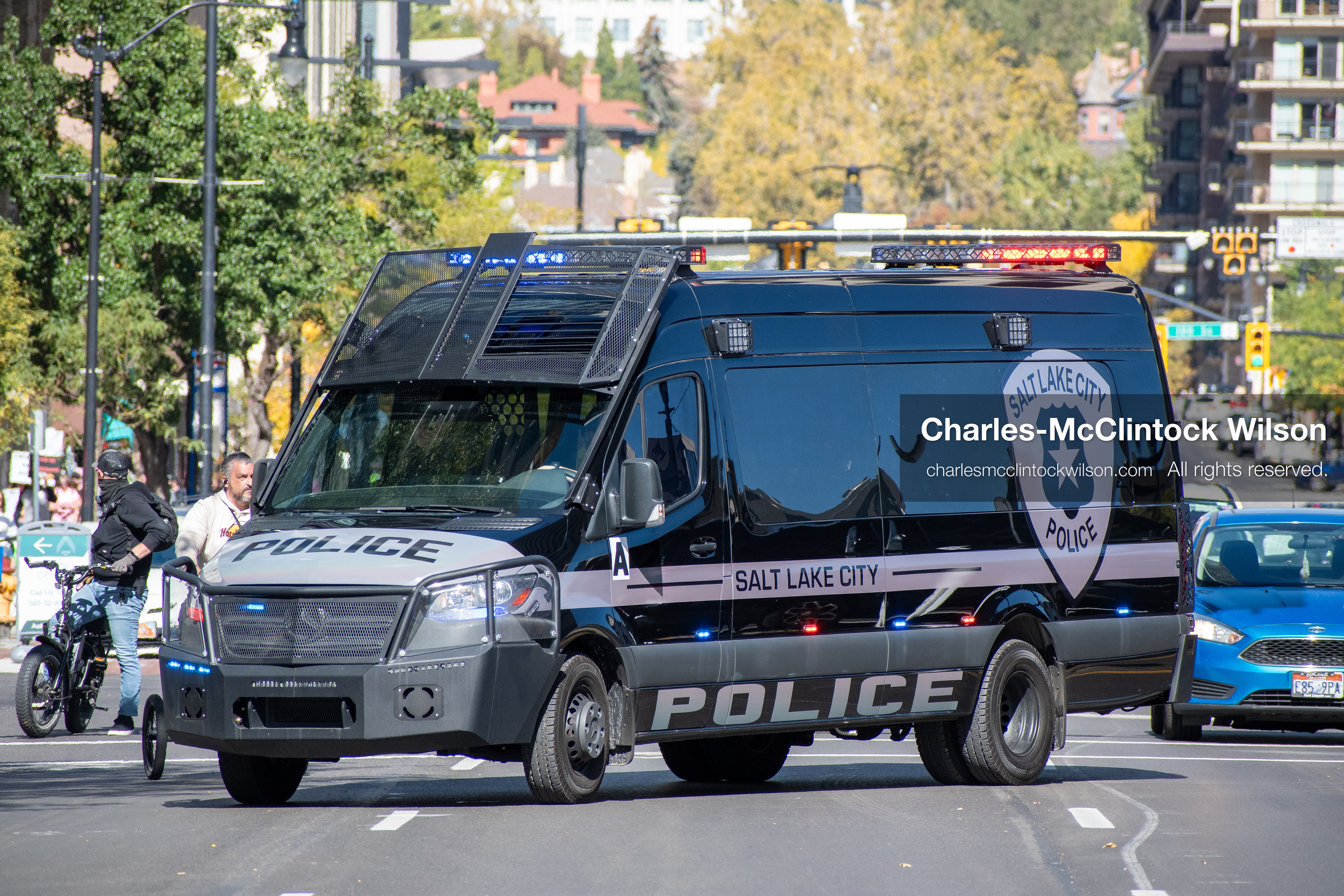October 18, 2025, Salt Lake City, Utah, USA: A police van drives past demonstrators during a "No Kings" protest on 14th Street in Salt Lake City, Utah. The protest was part of a nationwide mobilization.