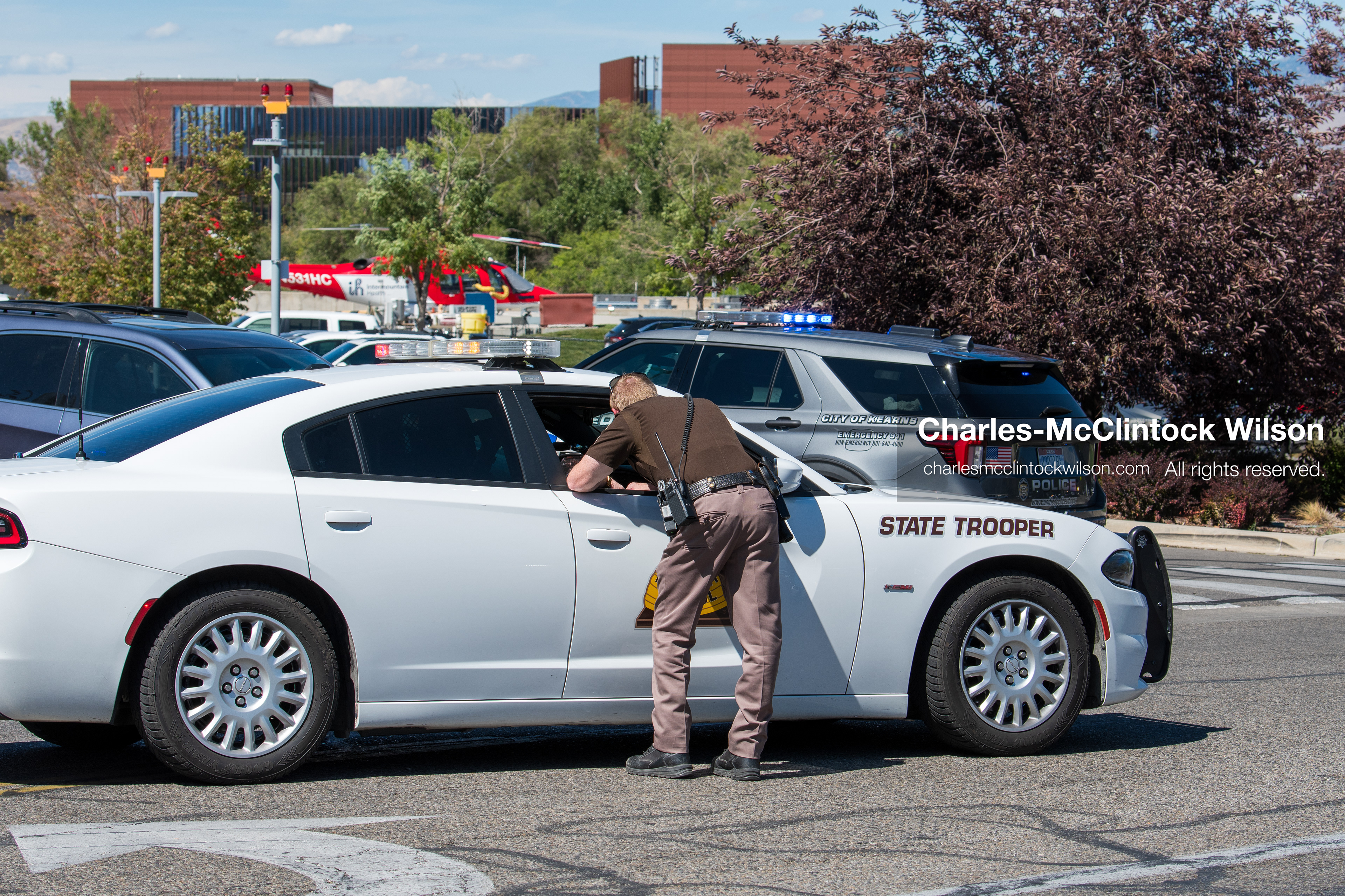 A Utah Highway Patrol trooper leans into the window of a marked state trooper cruiser outside Intermountain Medical Center in Murray, Utah, United States, on August 17, 2026. Multiple regional police agencies secured the hospital perimeter as a safety precaution after shooting victims were admitted following a fatal shootout outside a funeral service in nearby Kearns. (Photo by Charles-McClintock Wilson/NurPhoto)
