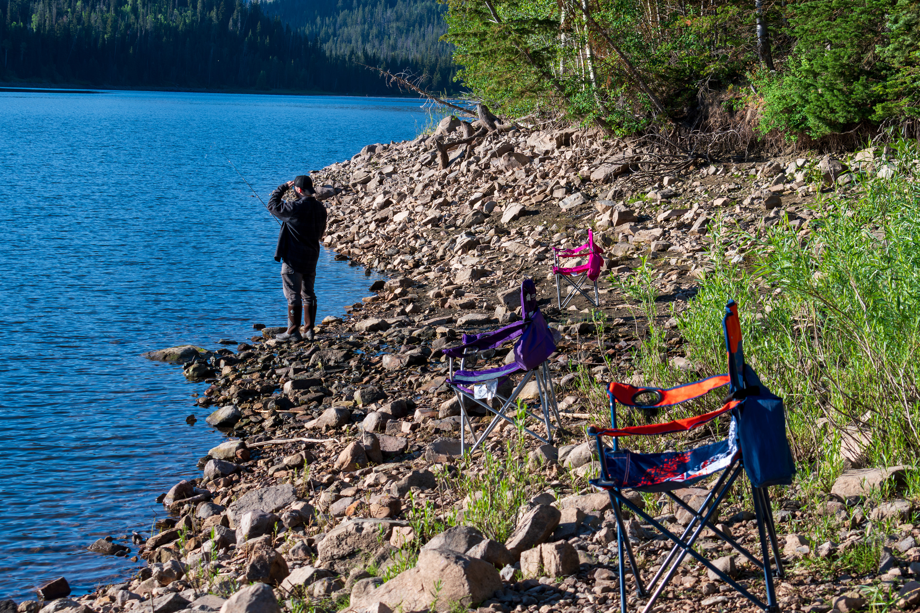 Summit County, Utah – July 20, 2025: A man fishes alone on the calm waters of Smith and Morehouse Reservoir during a quiet summer day.