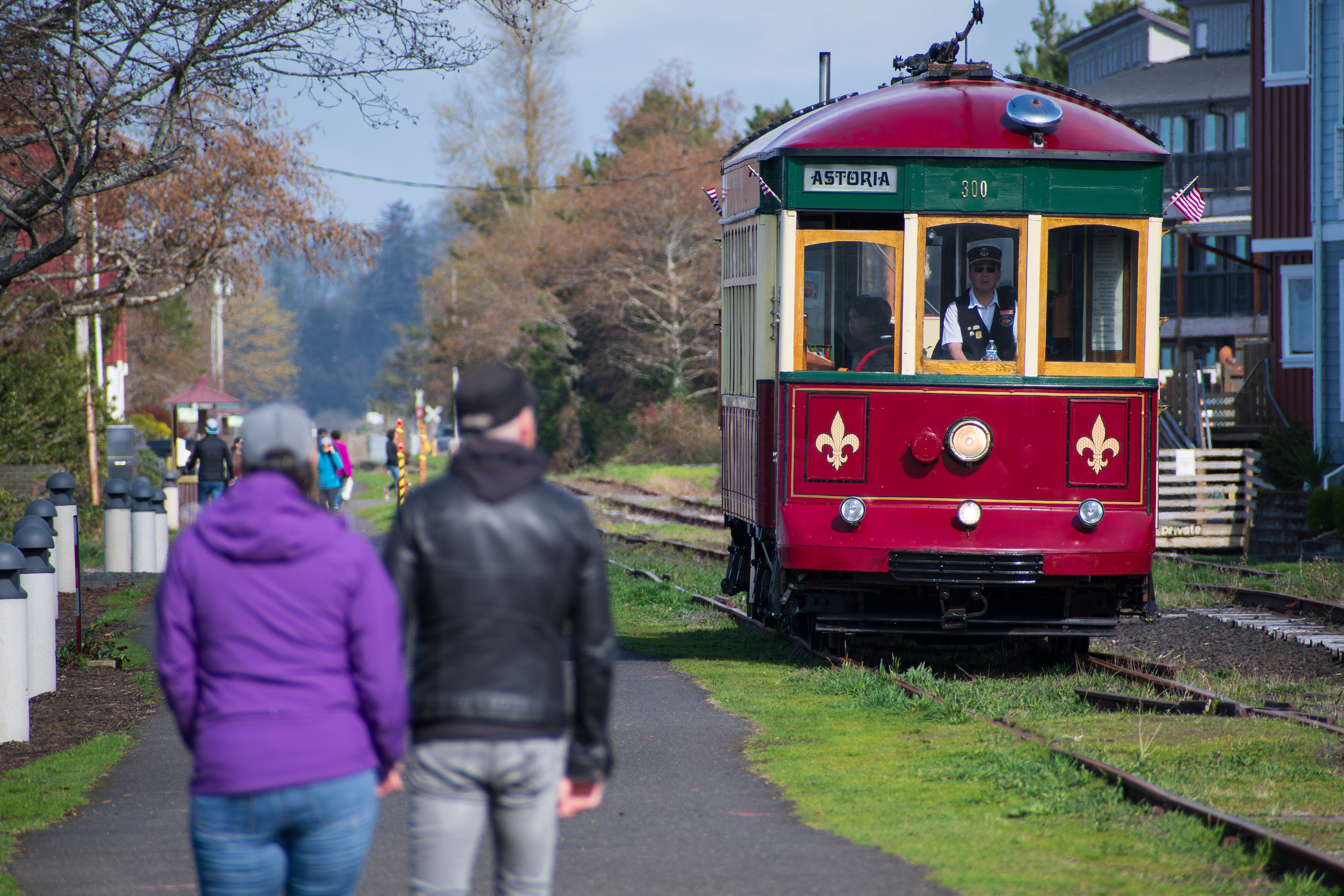 ASTORIA, OR, USA - APR 12, 2025: A couple walks along the Astoria Riverwalk as the Astoria Riverfront Trolley passes by, creating a dynamic scene along the Columbia River waterfront.