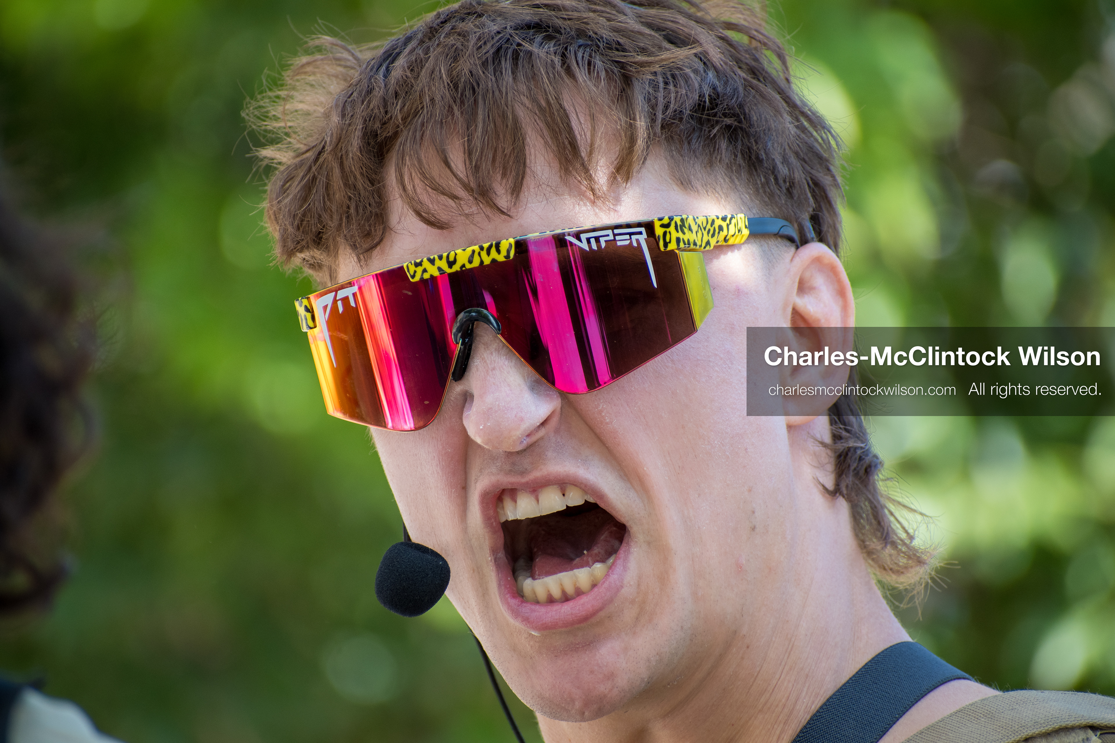 September 15, 2025 – Provo, Utah, United States: A demonstrator speaks emphatically into a headset microphone outside the Utah Valley Convention Center during a protest against the Department of Homeland Security career expo. Reflective “Pit Viper” sunglasses and a mullet hairstyle add visual intensity to the moment of civic expression. Photograph by Charles‑McClintock Wilson / ZUMA Press Wire