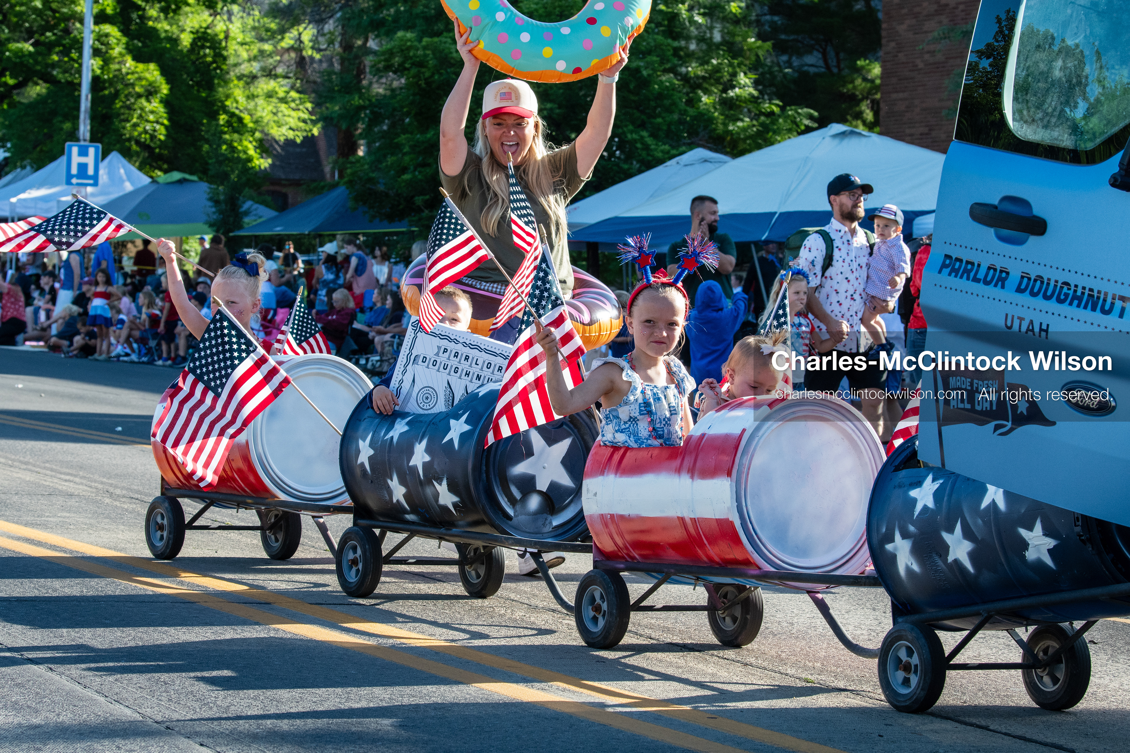 July 4, 2026, Provo, Utah, USA: Children ride in a barrel train decorated with a patriotic stars and stripes theme as a woman holds an inflatable donut beside a Parlor Doughnuts vehicle during America's Freedom Festival Grand Parade in Provo, Utah, Saturday, July 4, 2026. The annual Independence Day event features expanded programming to honor the 250th anniversary of United States independence. (Credit Image: © Charles-McClintock Wilson/ZUMA Press Wire)
