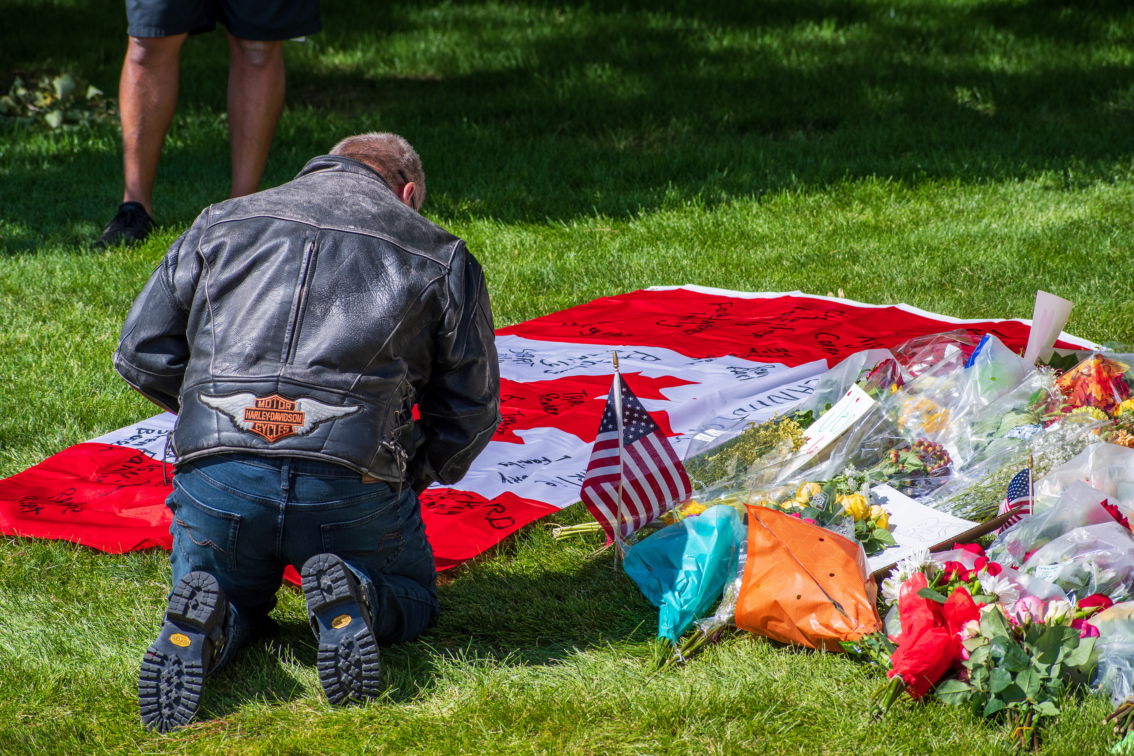 OREM, UTAH – SEPTEMBER 12, 2025: A man kneels beside a Canadian flag laid out on the grass at a memorial site for Charlie Kirk near Utah Valley University. Surrounded by bouquets, small American flags, and handwritten tributes, the scene reflects a moment of solemn remembrance. © Charles‑McClintock Wilson / ZUMA Press