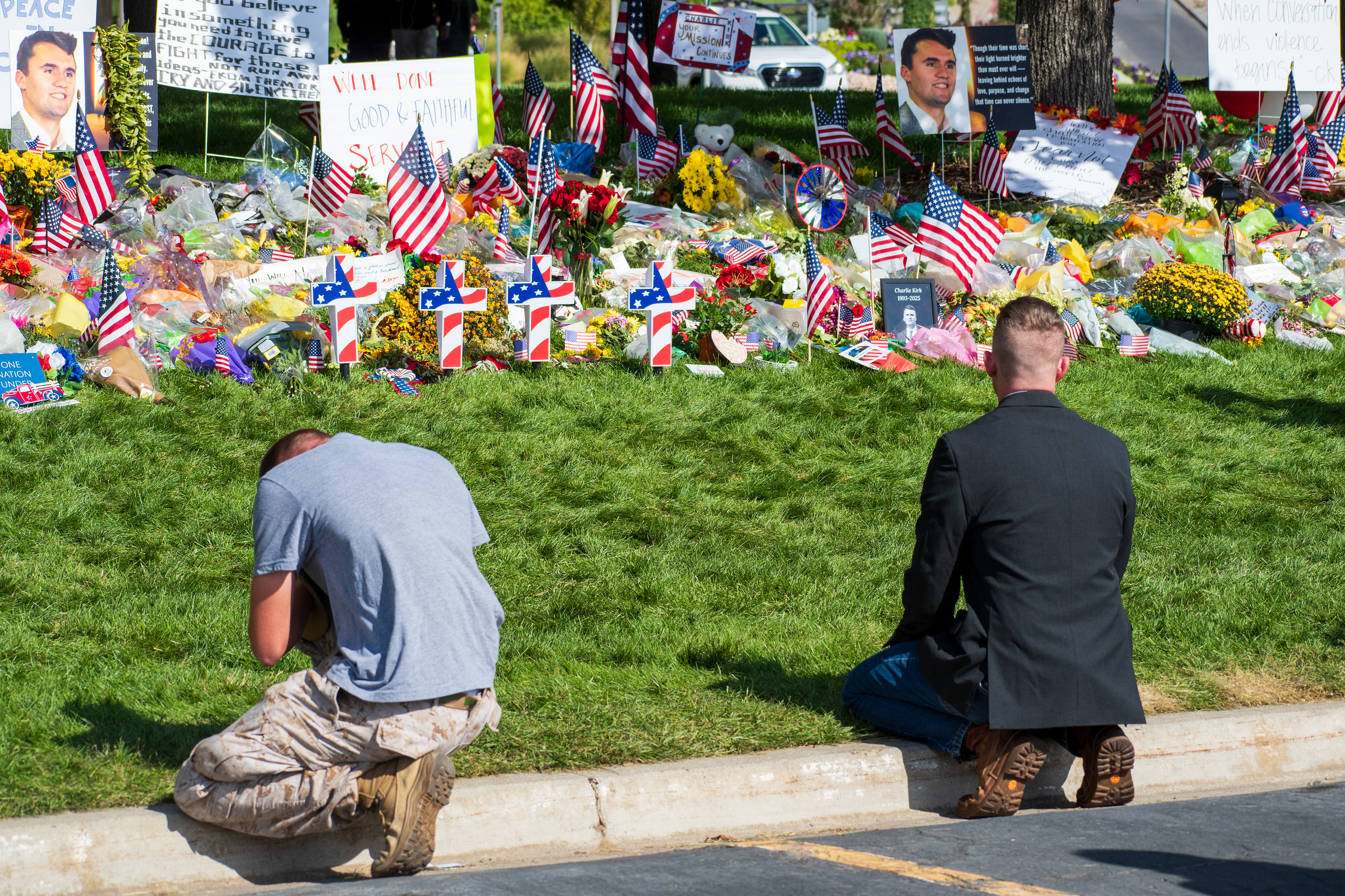 OREM, UTAH – SEPTEMBER 15, 2025: Two individuals kneel at a memorial site for Charlie Kirk on the campus of Utah Valley University. The tribute includes American flags, flowers, candles, and handwritten signs arranged around photographs and posters. © Charles‑McClintock Wilson / ZUMA Press